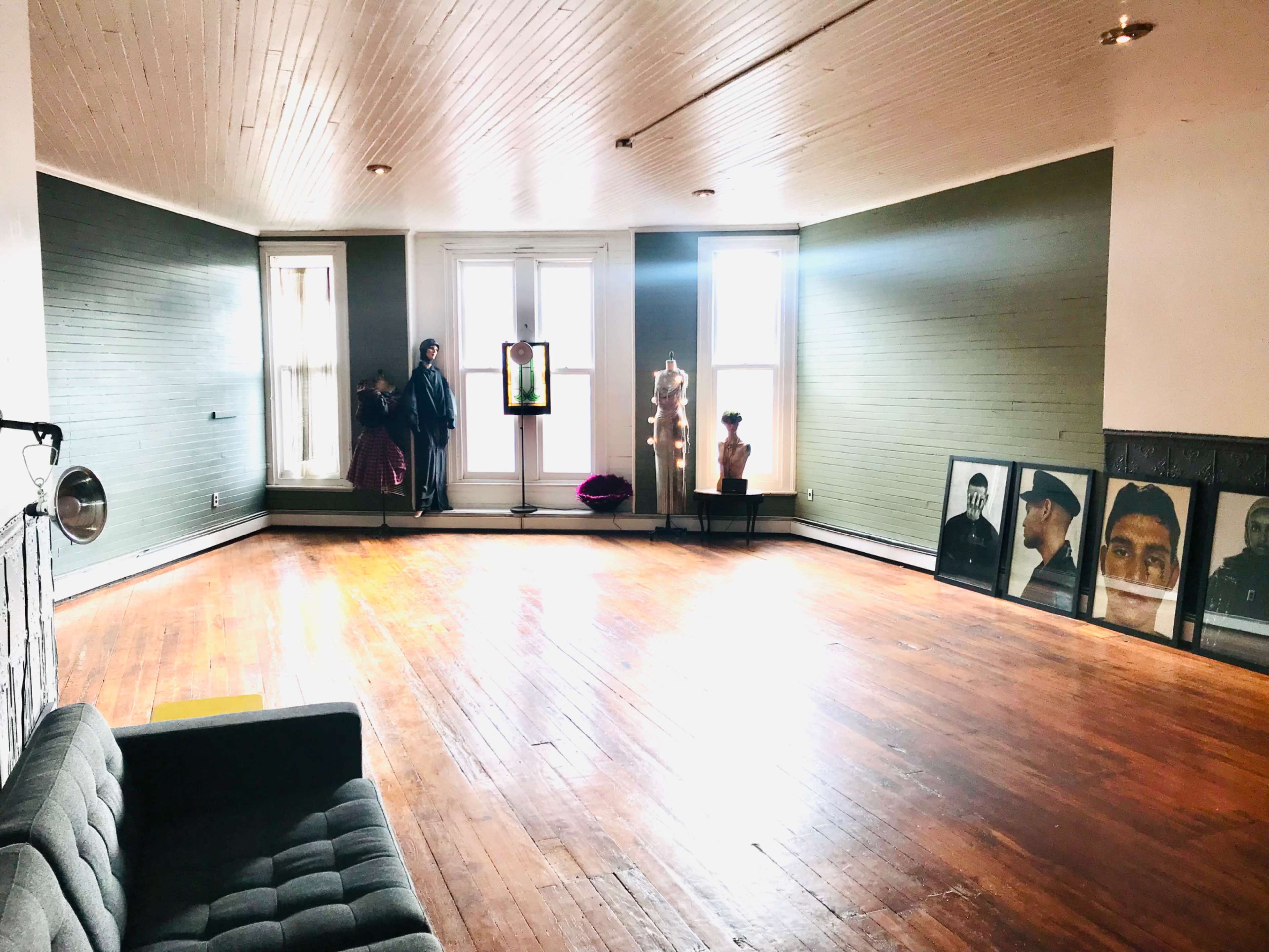 A spacious, empty room with wooden floors, large windows, and various artworks and mannequins displayed along the walls.