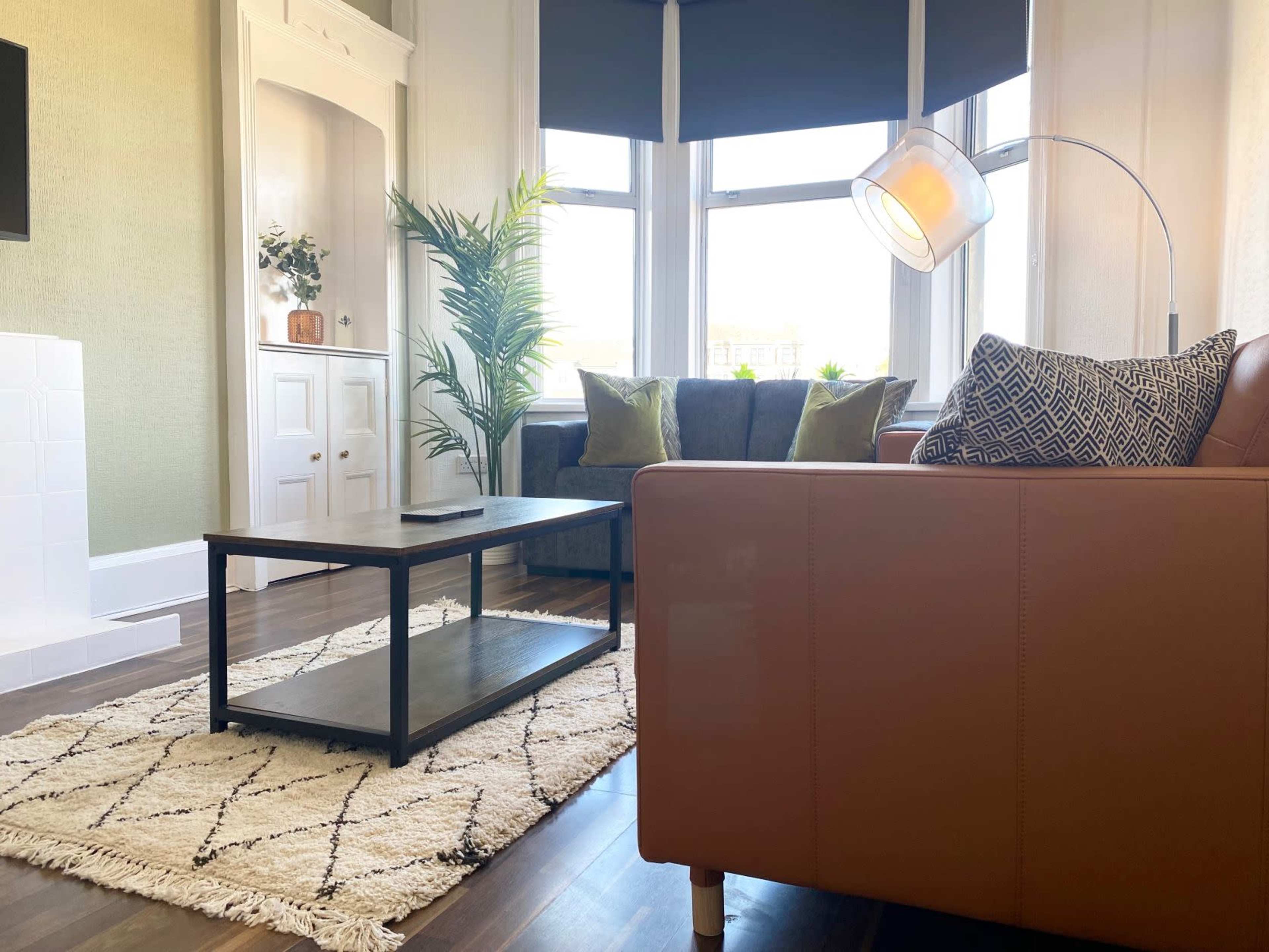 A living room with a brown leather couch, a coffee table, a patterned area rug, and large windows allowing natural light.