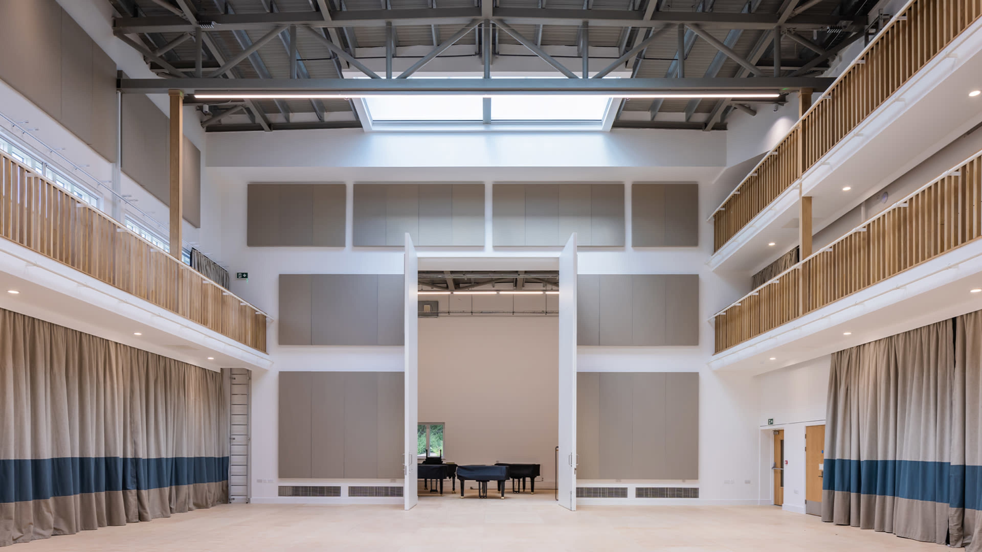 A spacious room with high ceilings, large foldable panels, and a grand piano placed in the center.