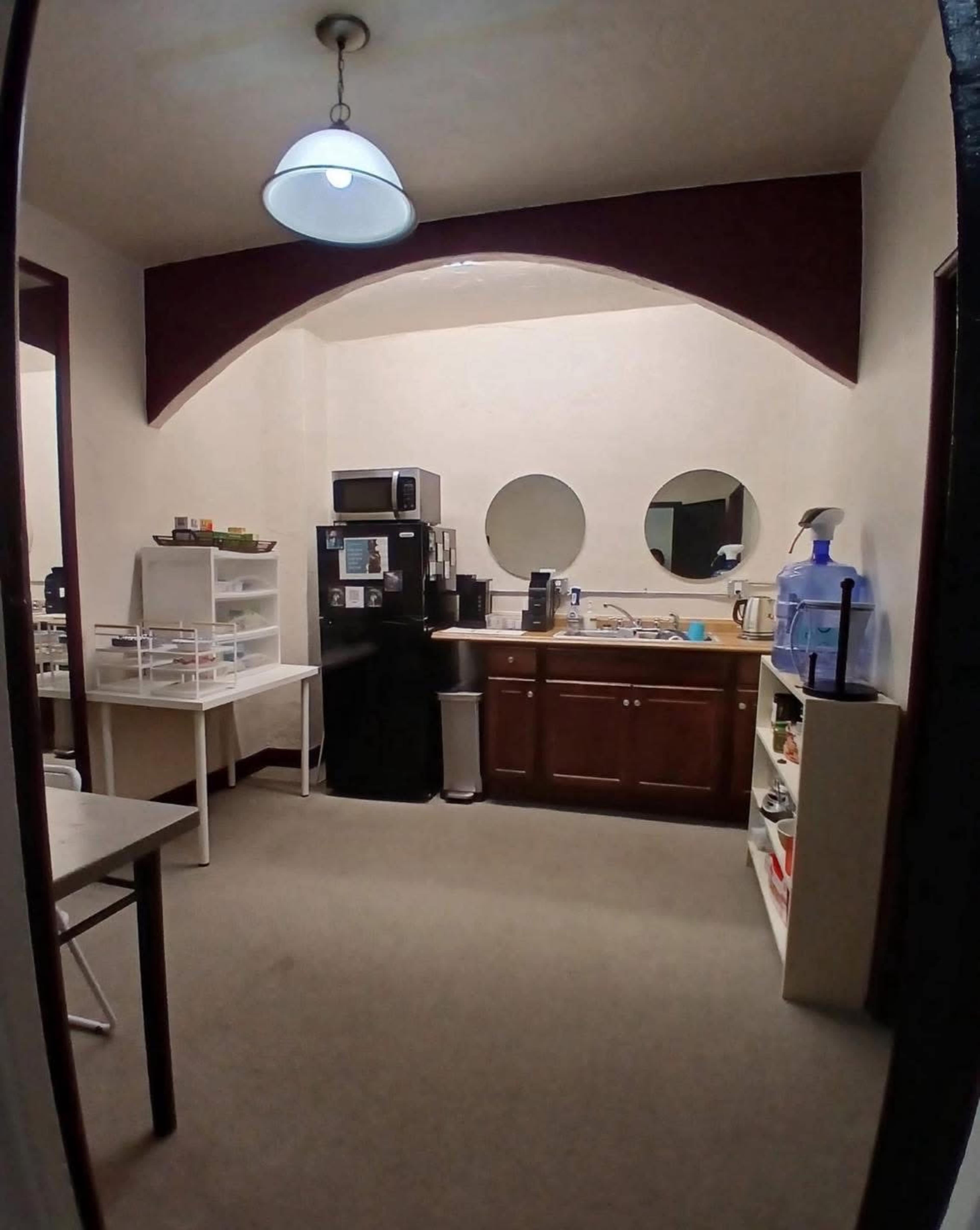 The image shows a small kitchen with a refrigerator, microwave, sink, and various shelves arranged along the walls.