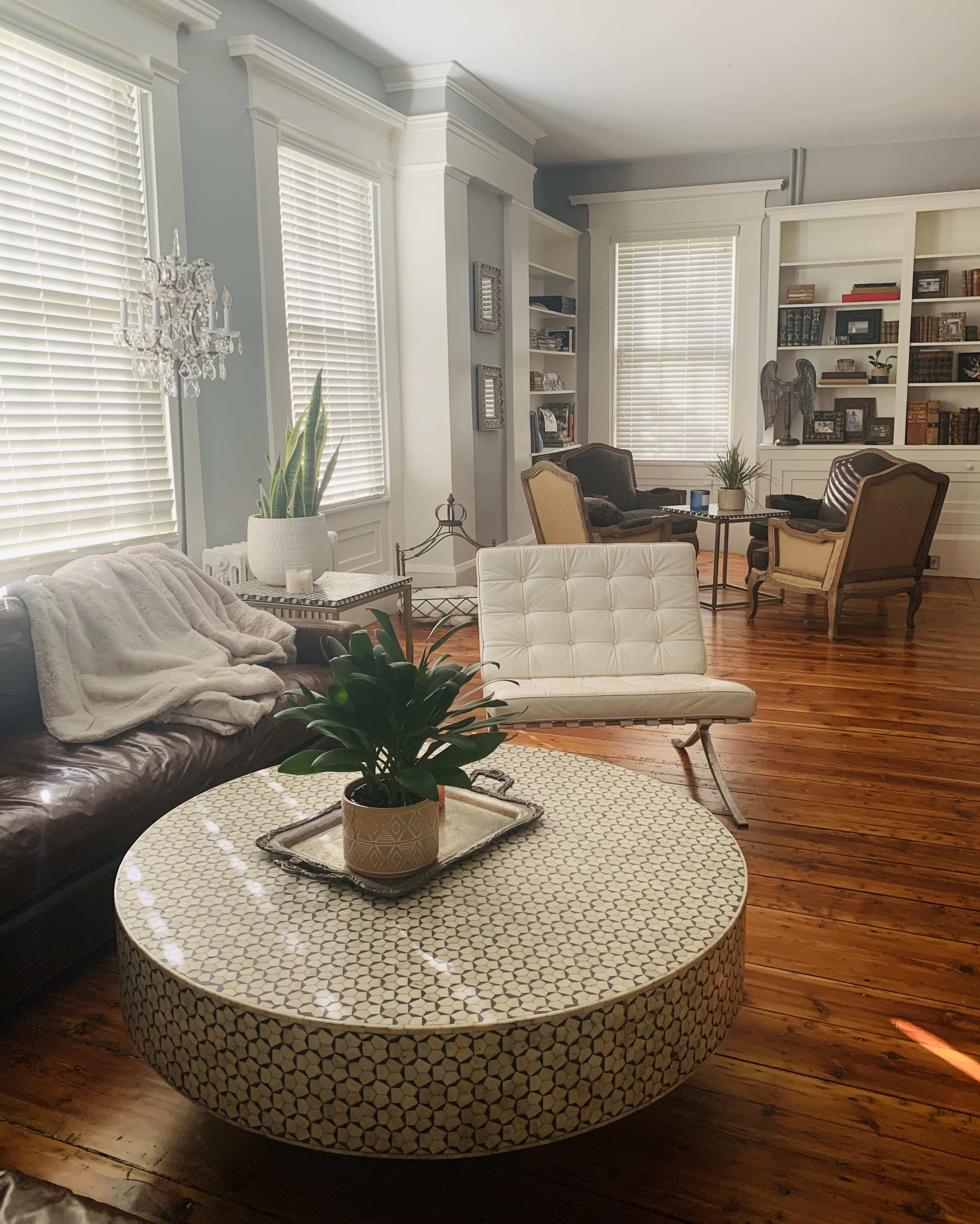 The living room features a circular, patterned coffee table surrounded by a leather sofa, armchairs, and bookshelves filled with books.