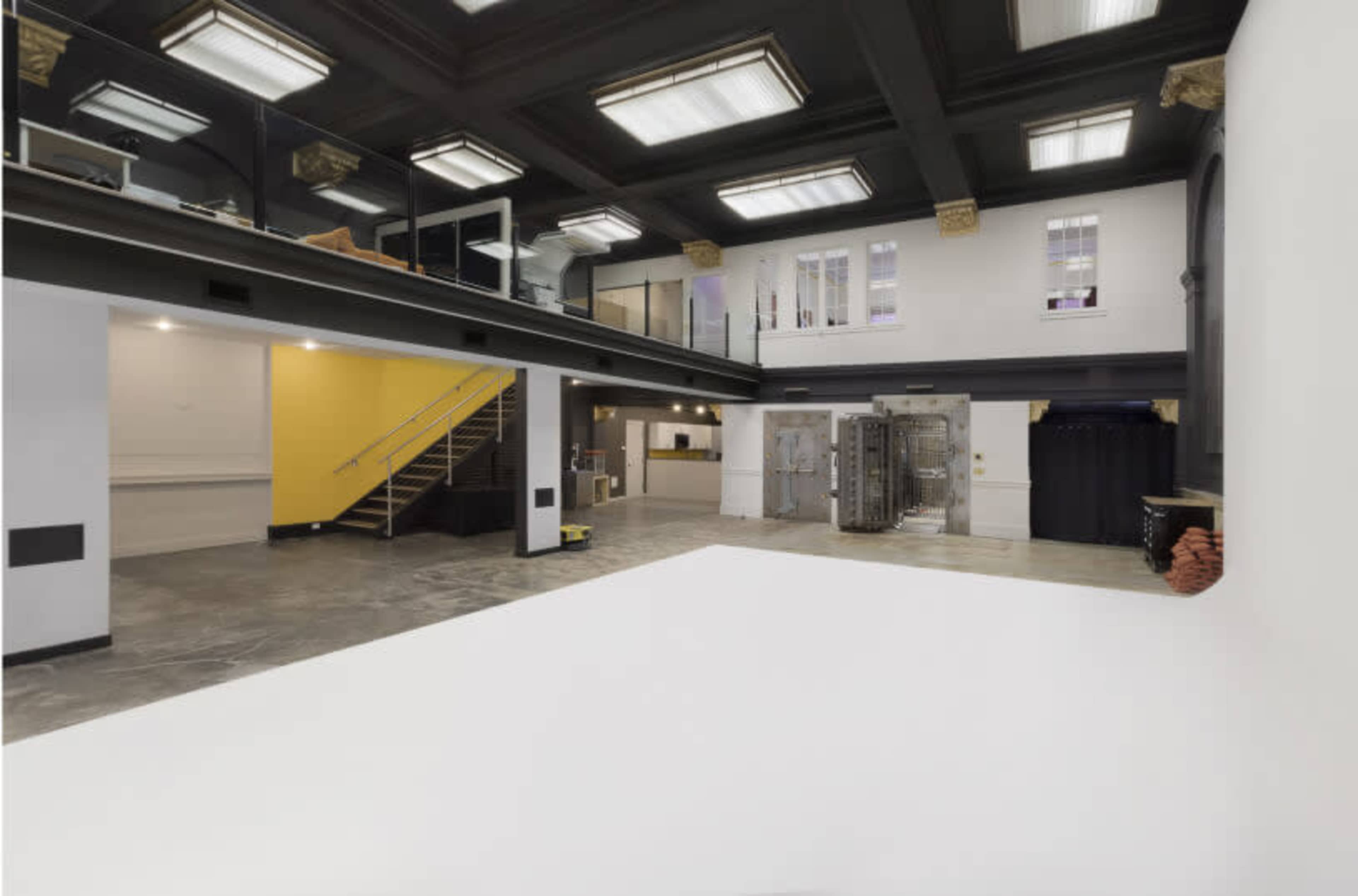 A spacious, modern interior with a lofted area, a large white floor space, and a staircase leading to an upper level.