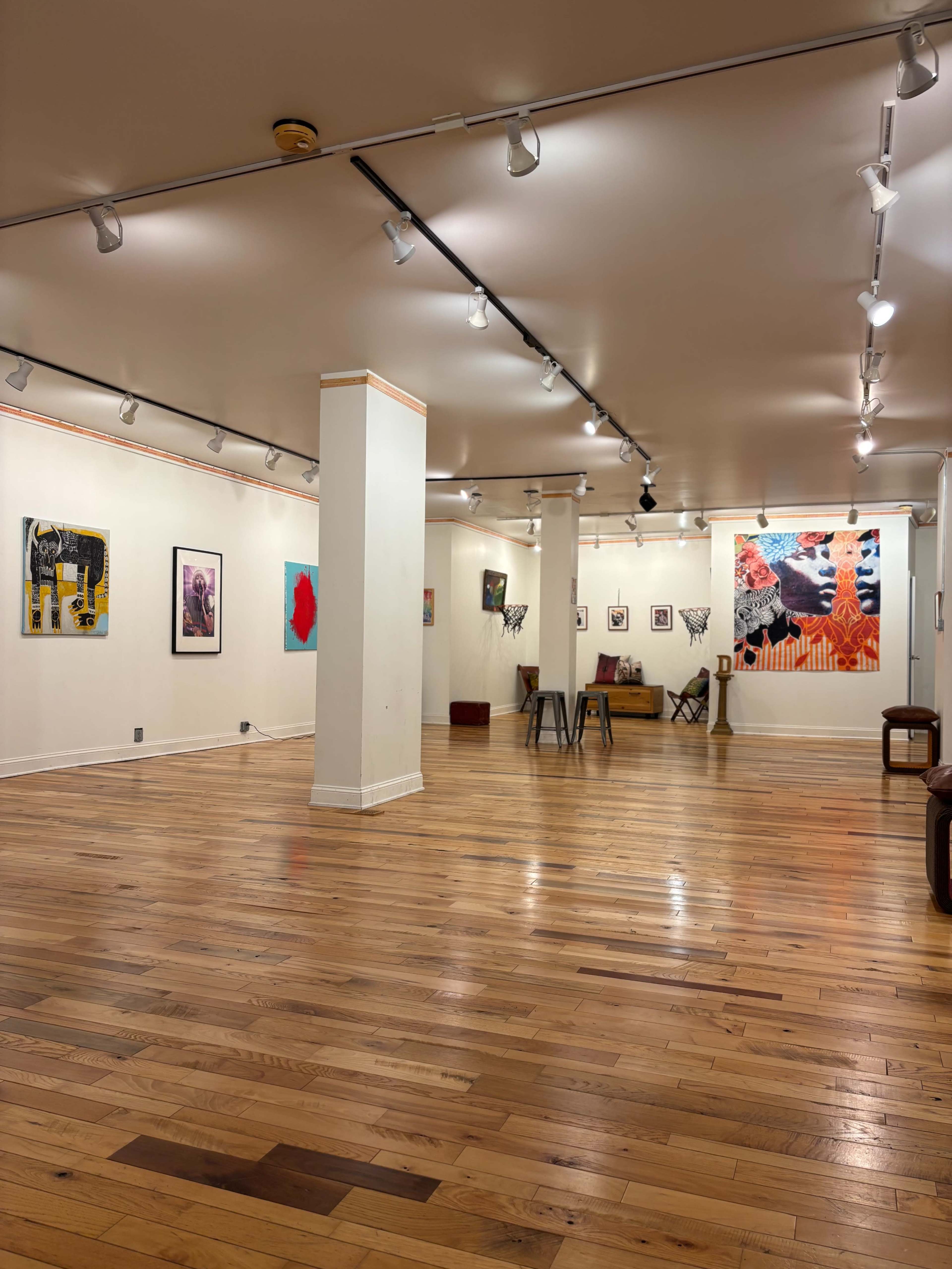 The image shows an empty art gallery featuring several framed artworks on white walls and polished wooden flooring.