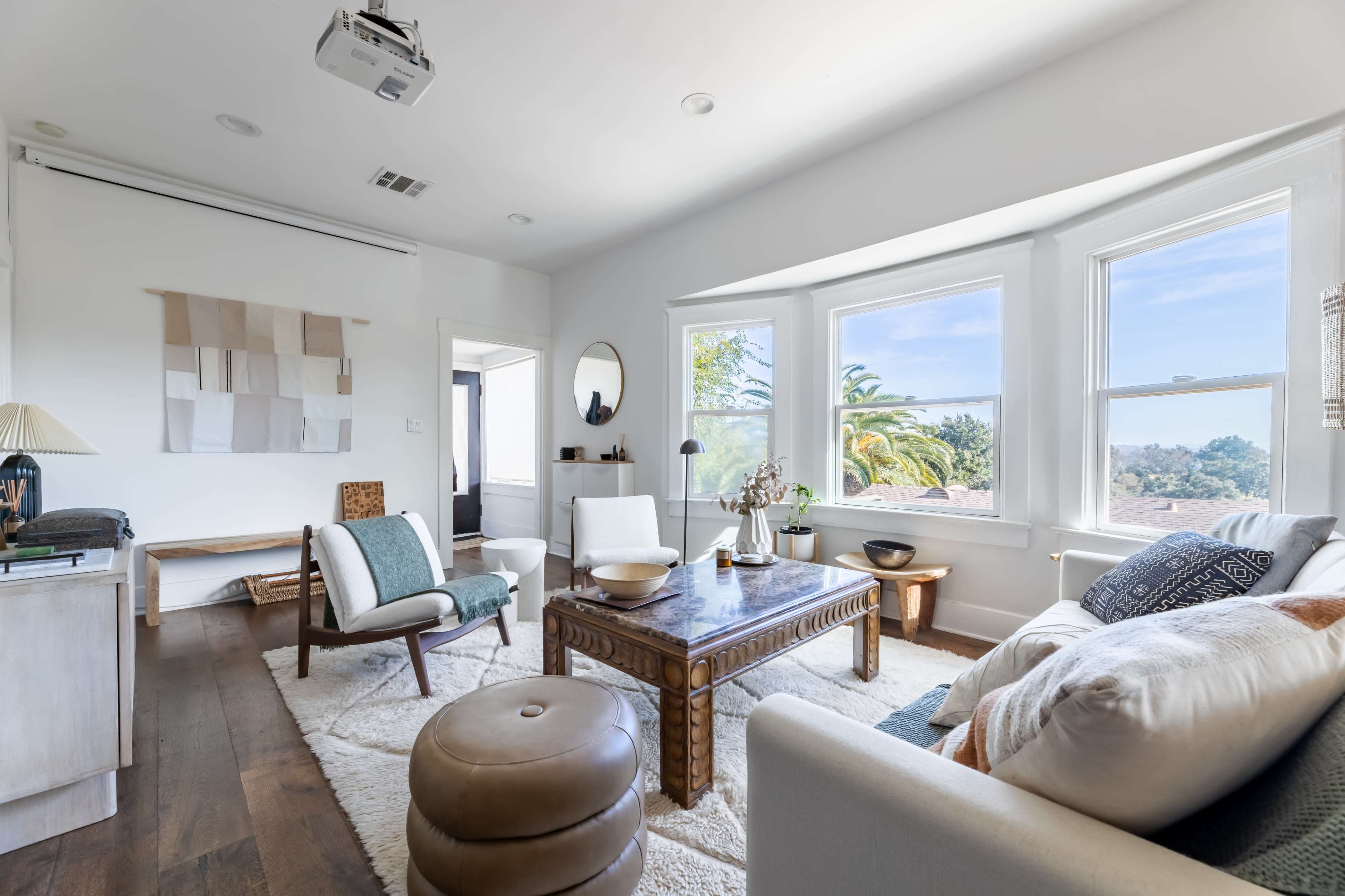 The living room features a sectional sofa, wooden coffee table, and natural light streaming through large windows.