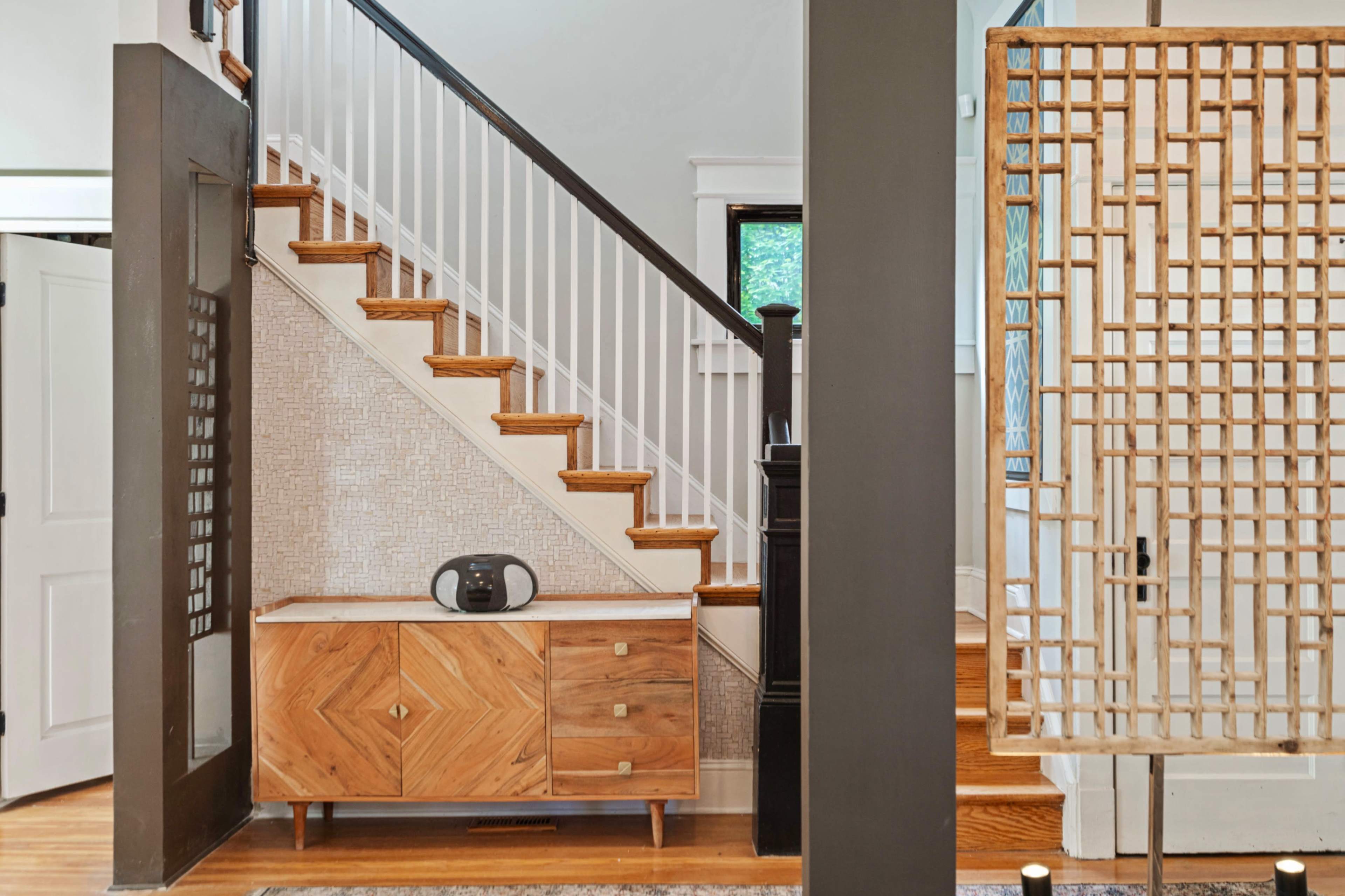 A foyer with a wooden staircase on the right, a patterned wall beside the stairs, and a decorative wooden screen separating the space.