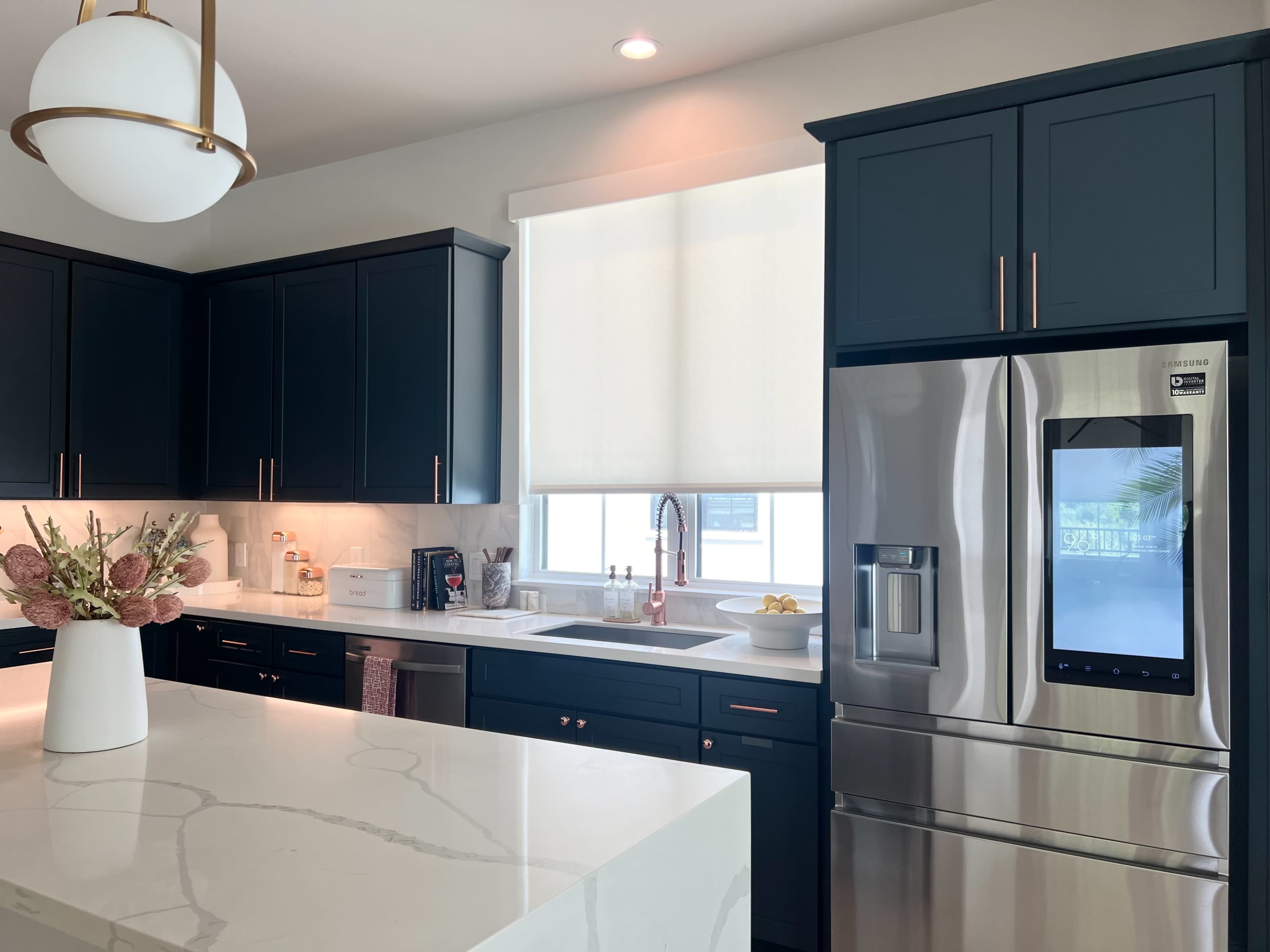 A modern kitchen features dark cabinets, a stainless steel refrigerator, and a white marble countertop with a floral arrangement.