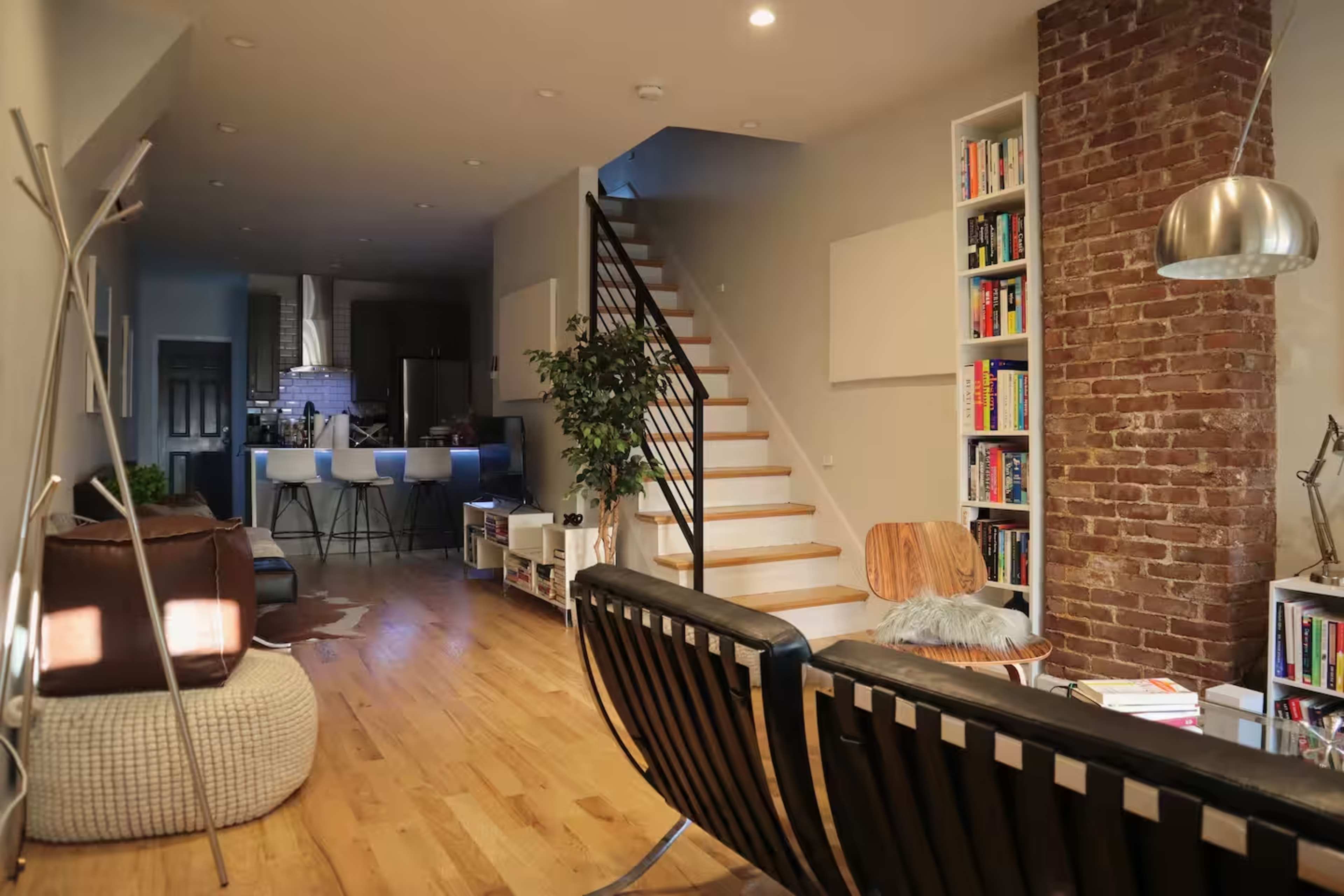 An inviting, open-concept living space features a modern seating area, a staircase leading to upper levels, and a view into a kitchen with bar stools.