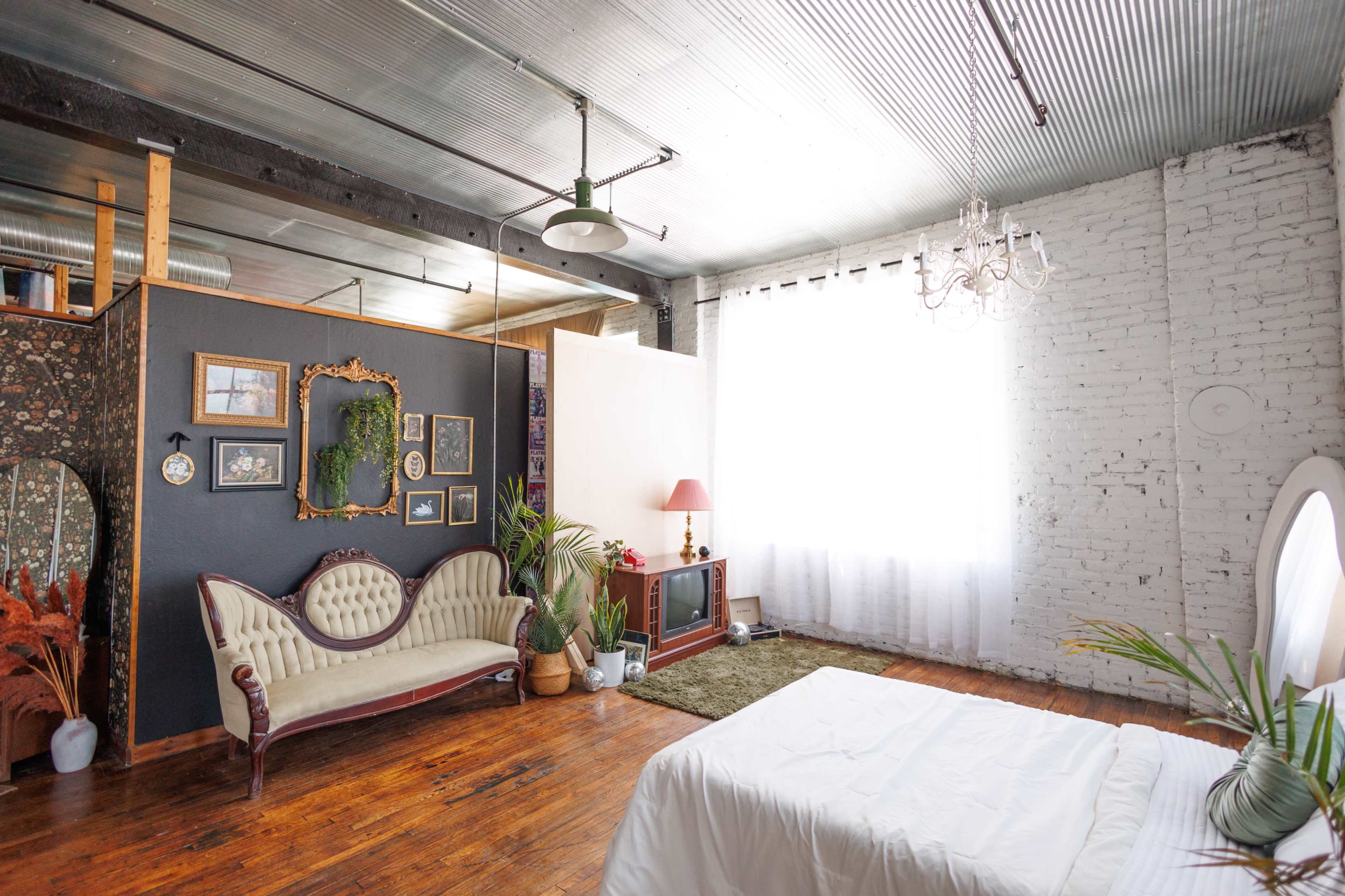 The image shows a spacious room featuring a vintage sofa, a chandelier, and large windows with light streaming in.