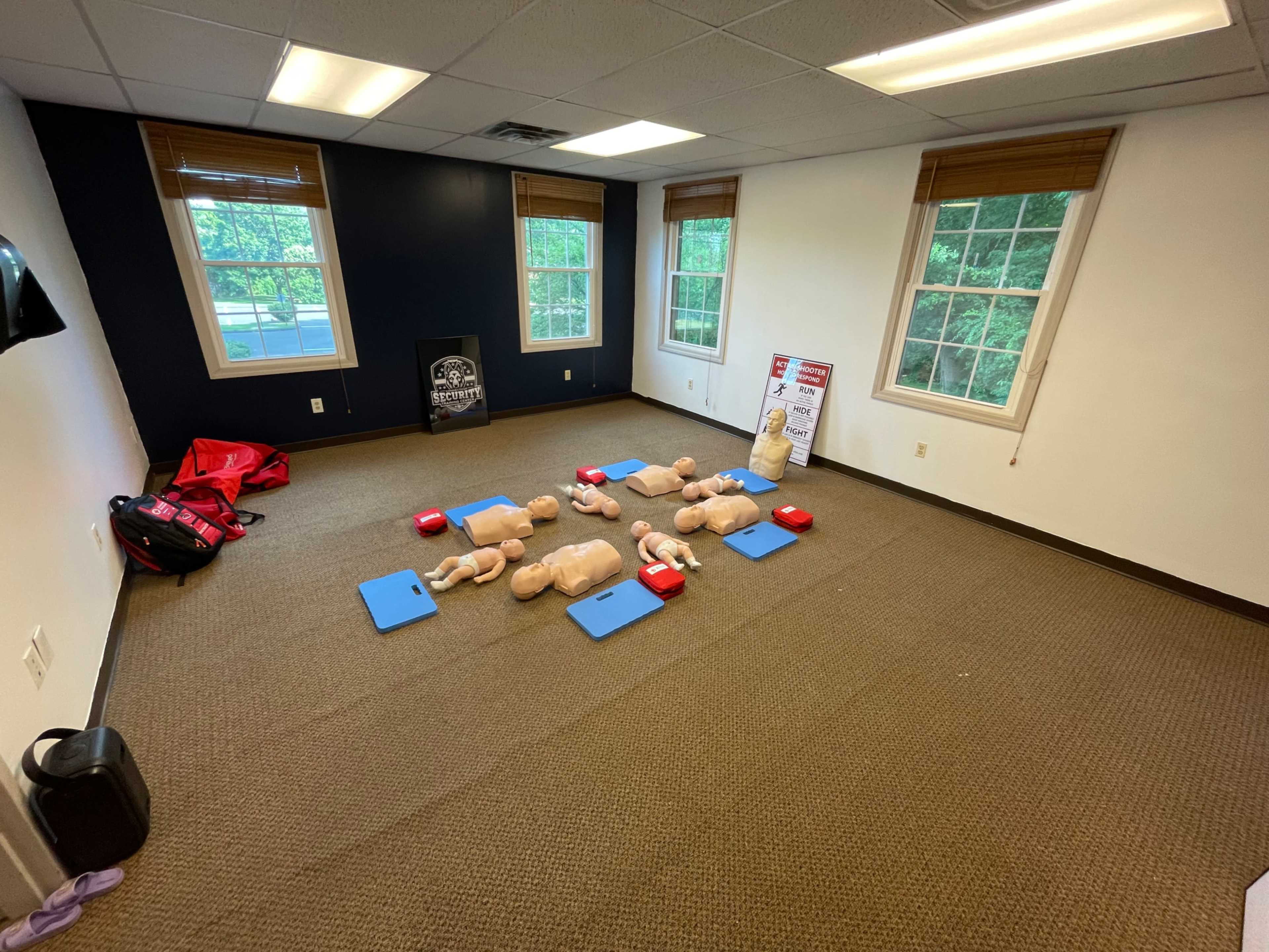 The image shows a room set up for CPR training, with several mannequins, CPR training pads, and instructional materials arranged on the floor.