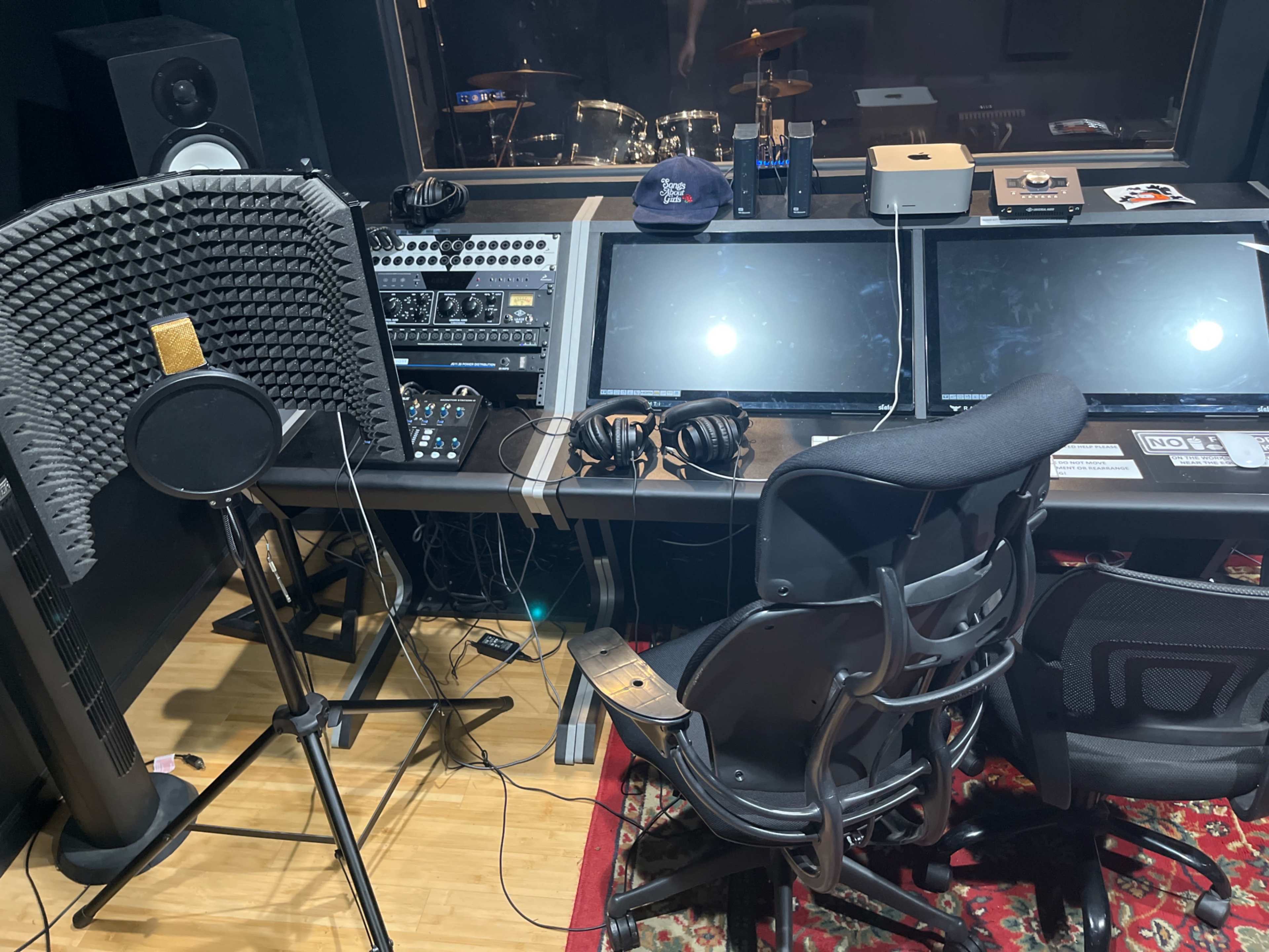 A recording studio setup with two computer monitors, a microphone, headphones, and various audio equipment arranged on a desk.