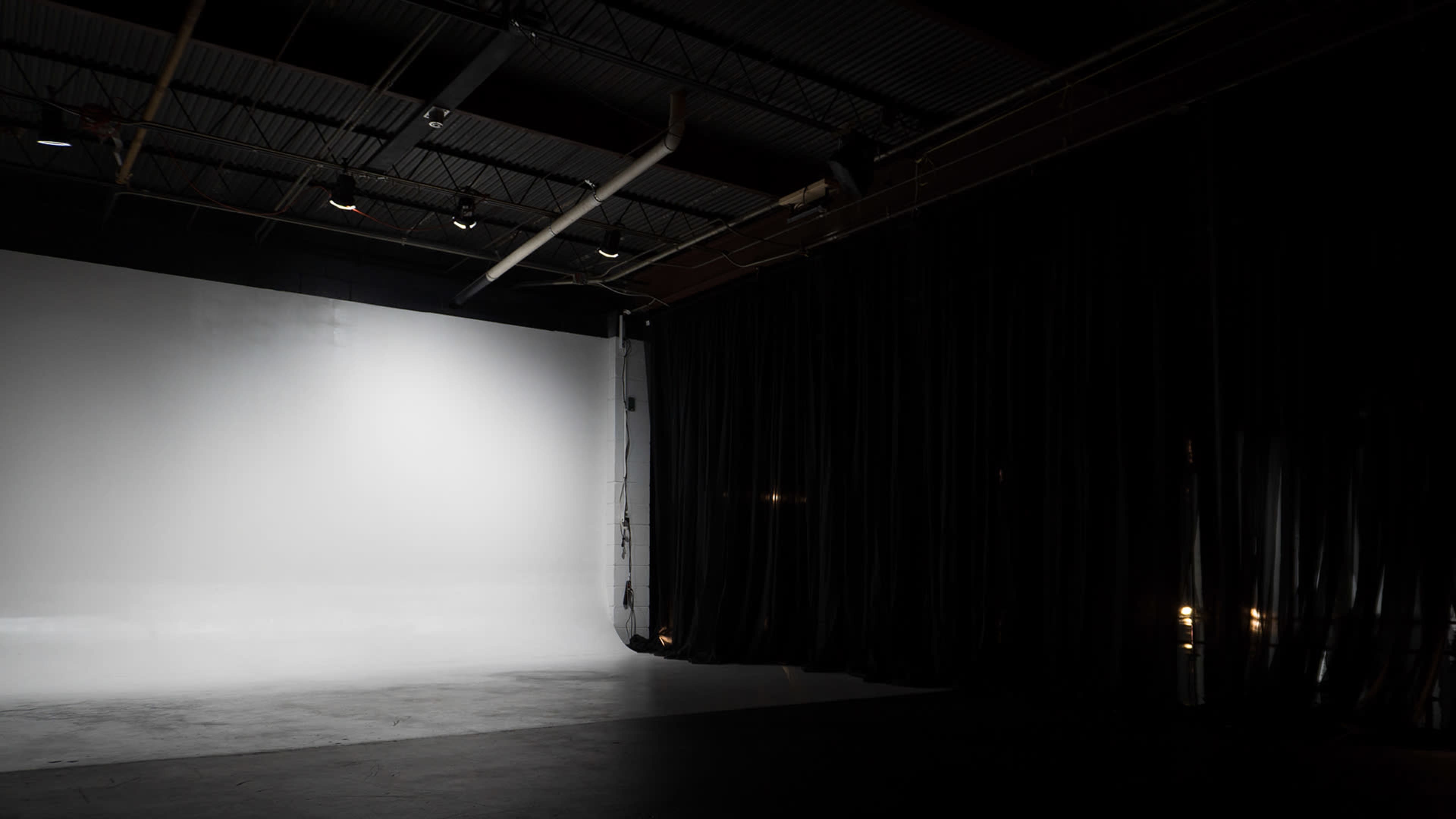 The image shows a spacious photography studio with a large white backdrop and dark curtains along one side.