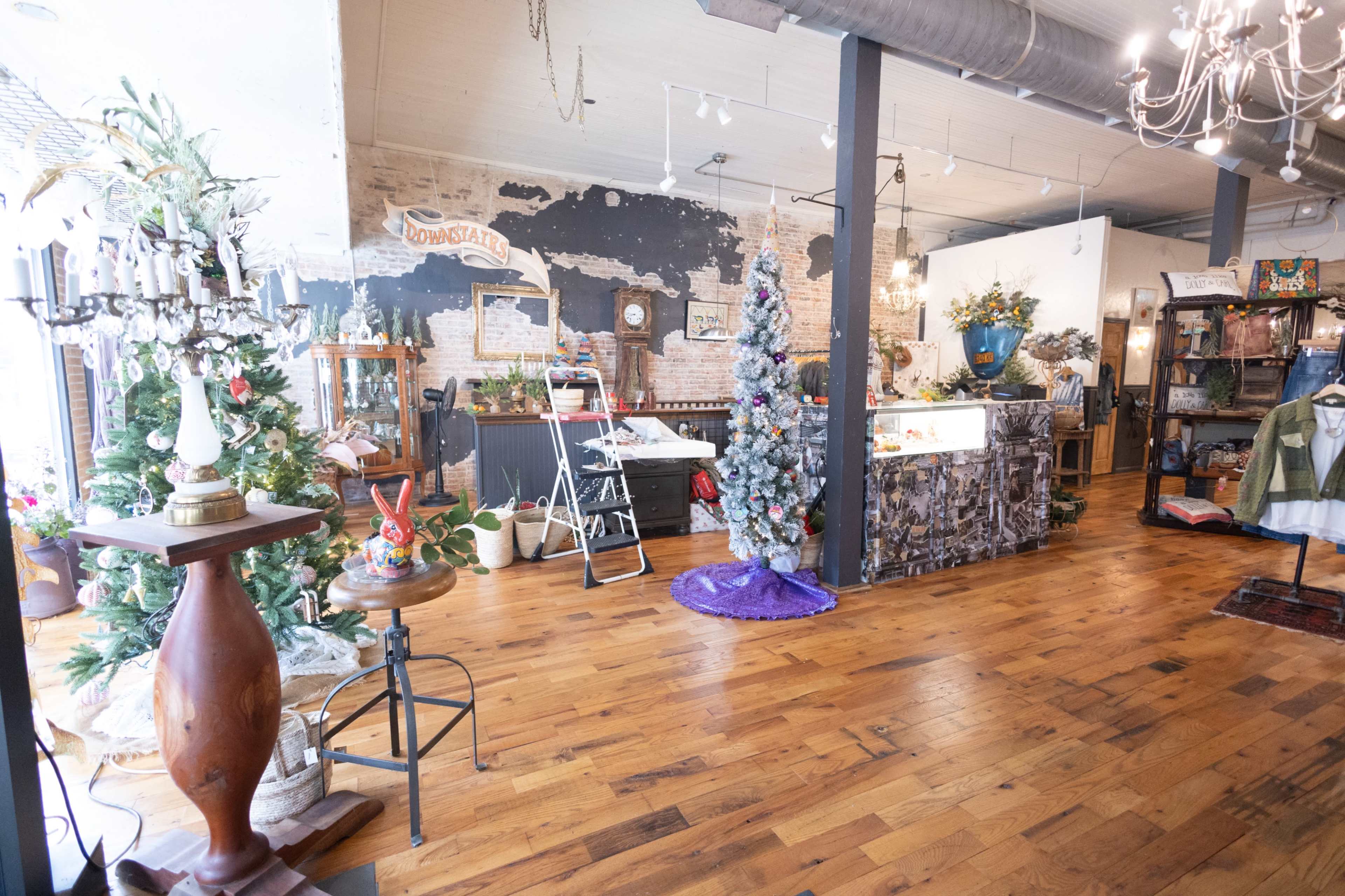 The interior of a rustic shop features wooden flooring, a decorated Christmas tree, and various vintage furniture items arranged around a display counter.