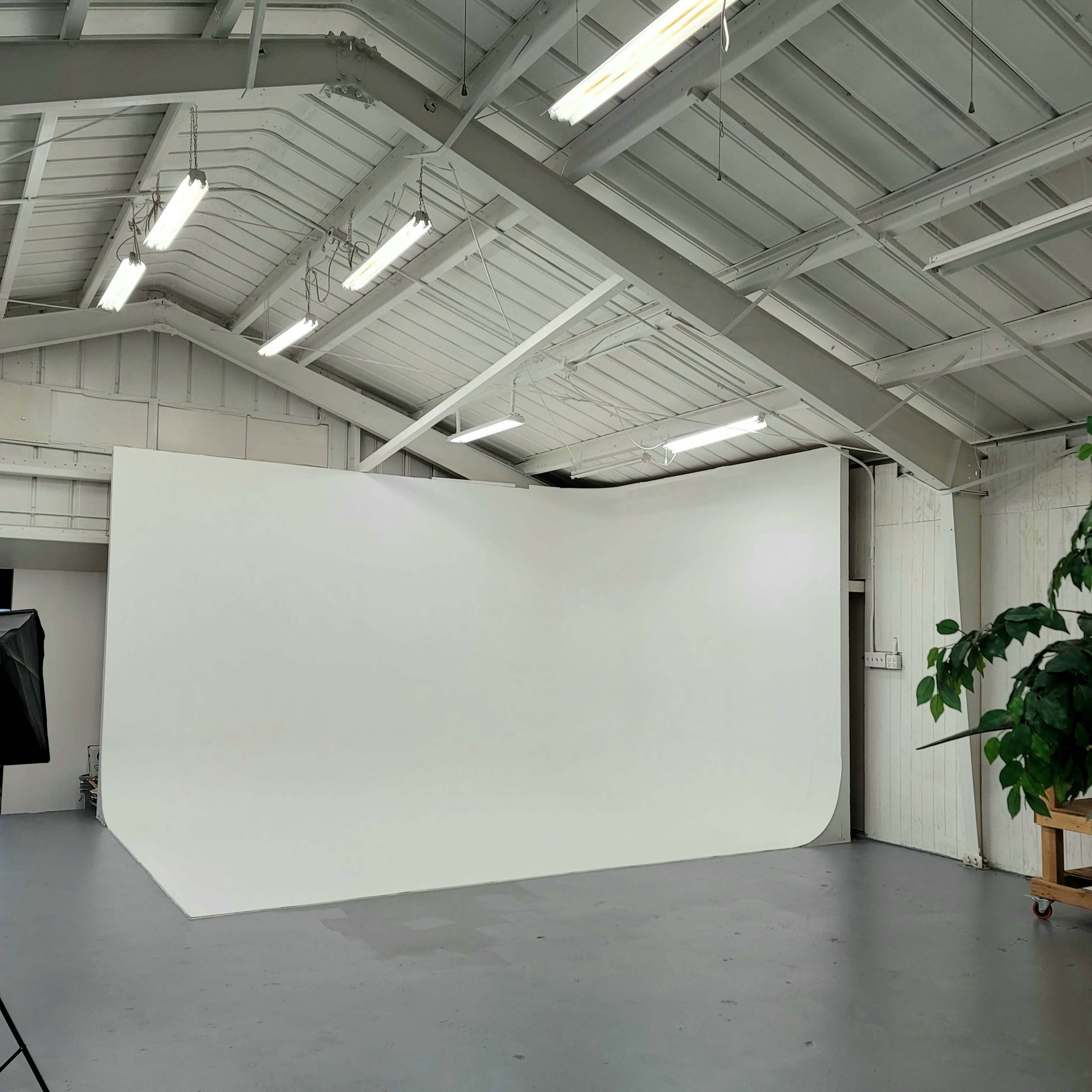 A spacious studio with a large, curved white backdrop and high ceilings, illuminated by overhead lights.