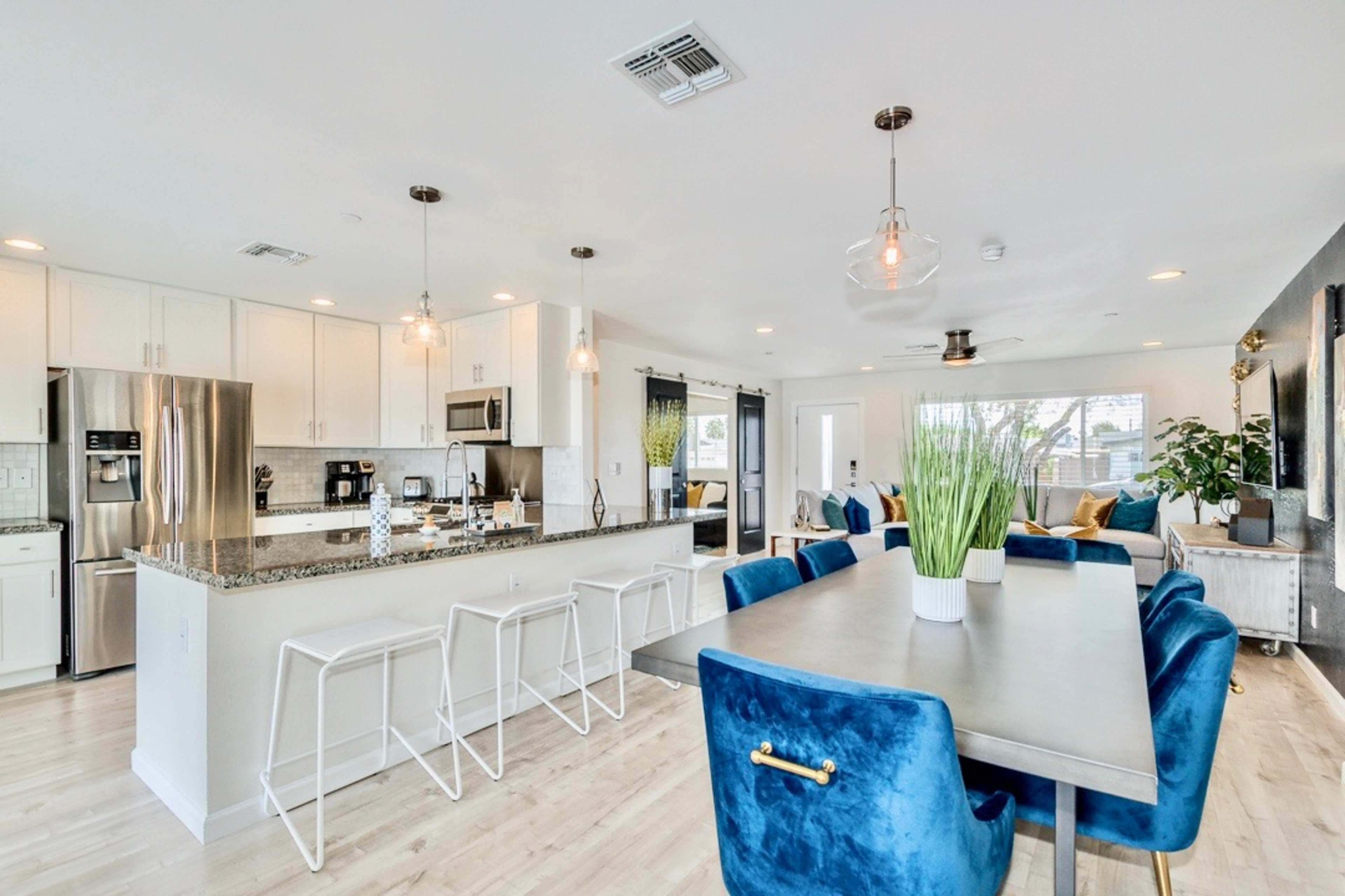 A modern kitchen and dining area features a large table surrounded by blue chairs, with an island bar and stainless steel appliances in a bright, open space.
