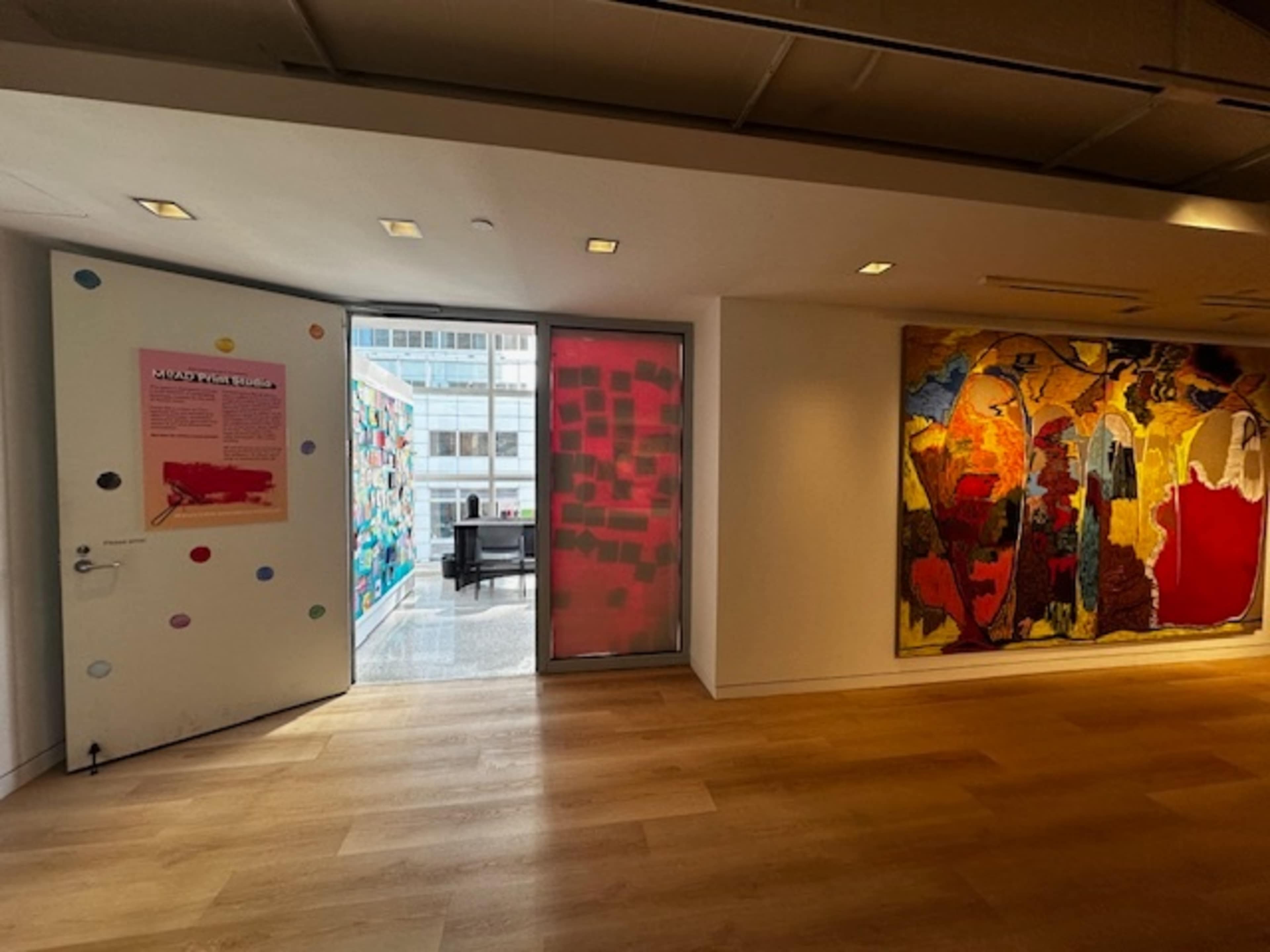A doorway opens to a patio area with colorful murals, alongside a large abstract painting on the wall inside the gallery.