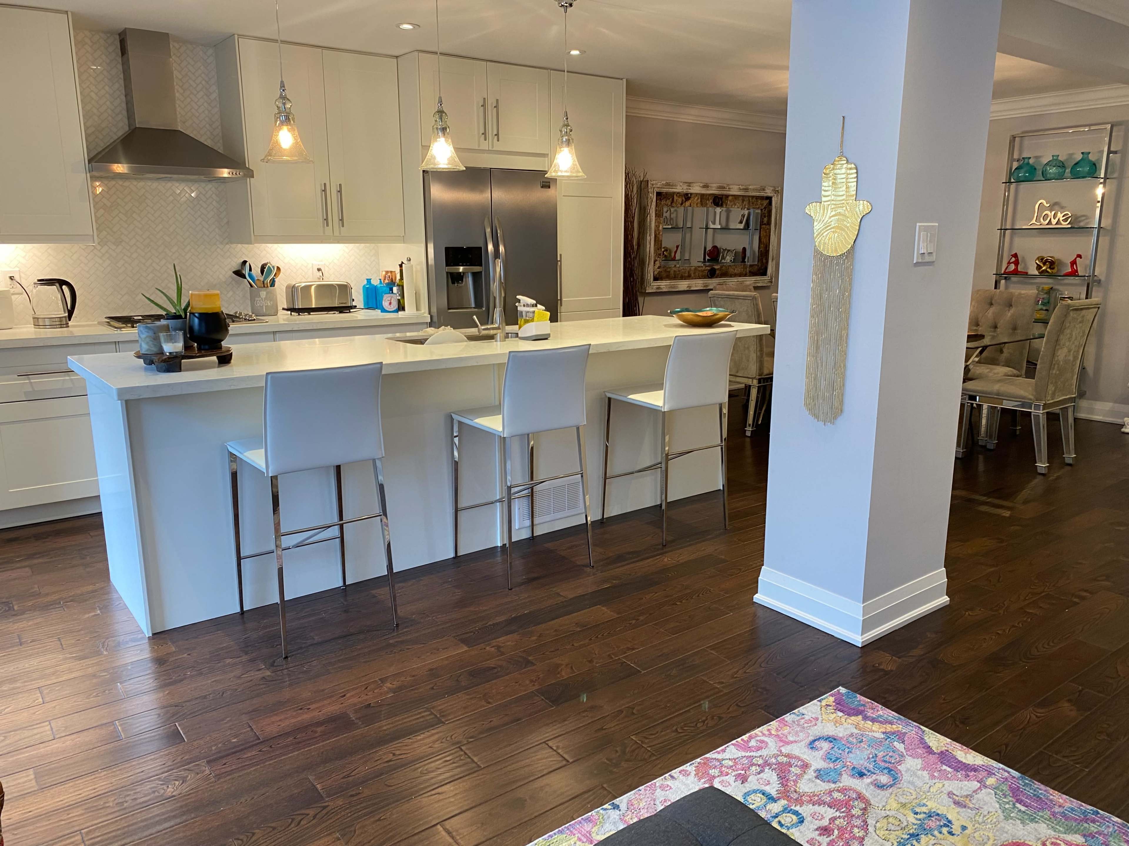 A modern kitchen with white cabinetry, a central island with bar stools, and hardwood flooring.