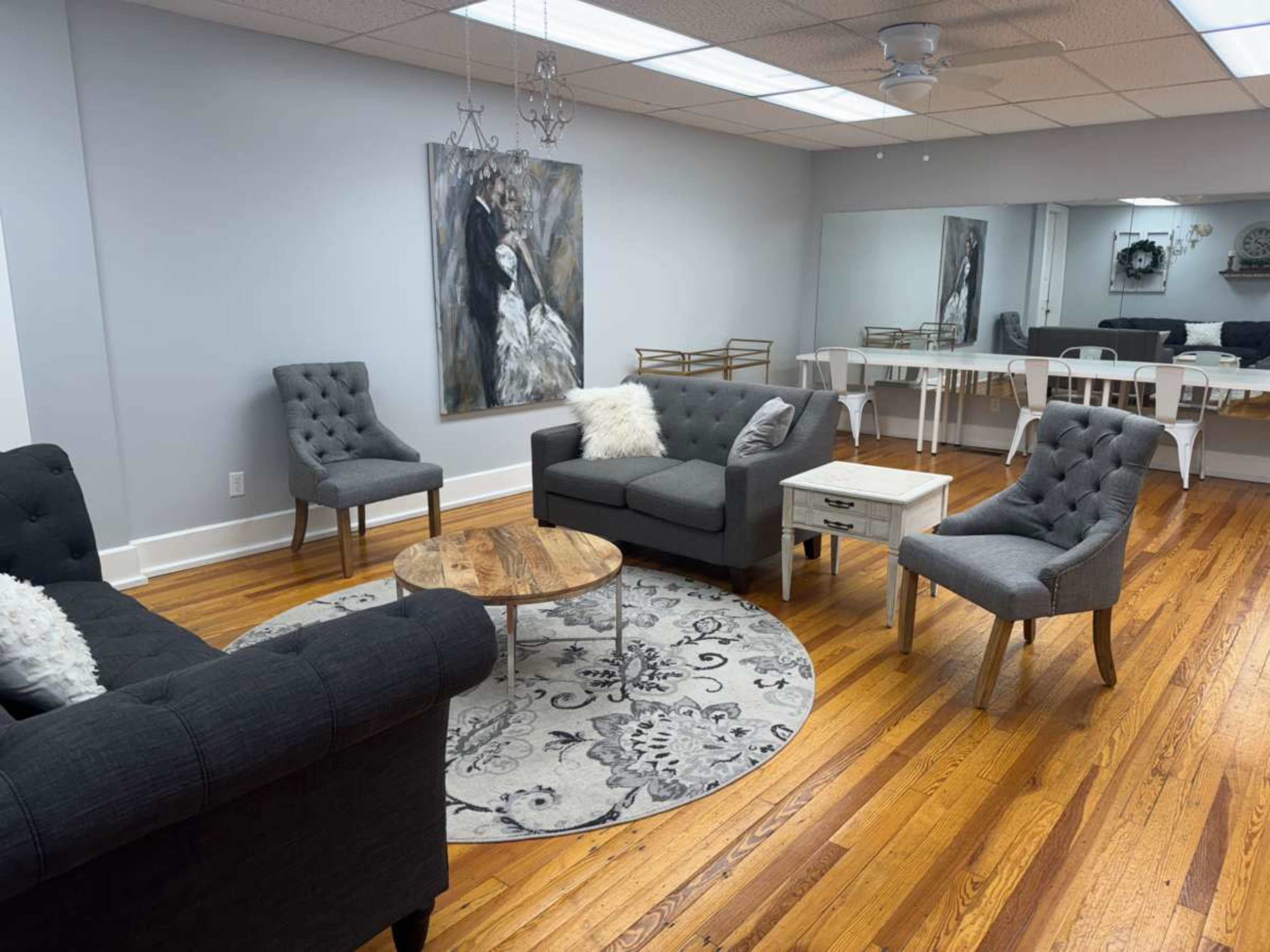 The image shows a modern lounge area with gray furniture, a circular area rug, and a wooden coffee table, complemented by a large wall painting and mirrors.