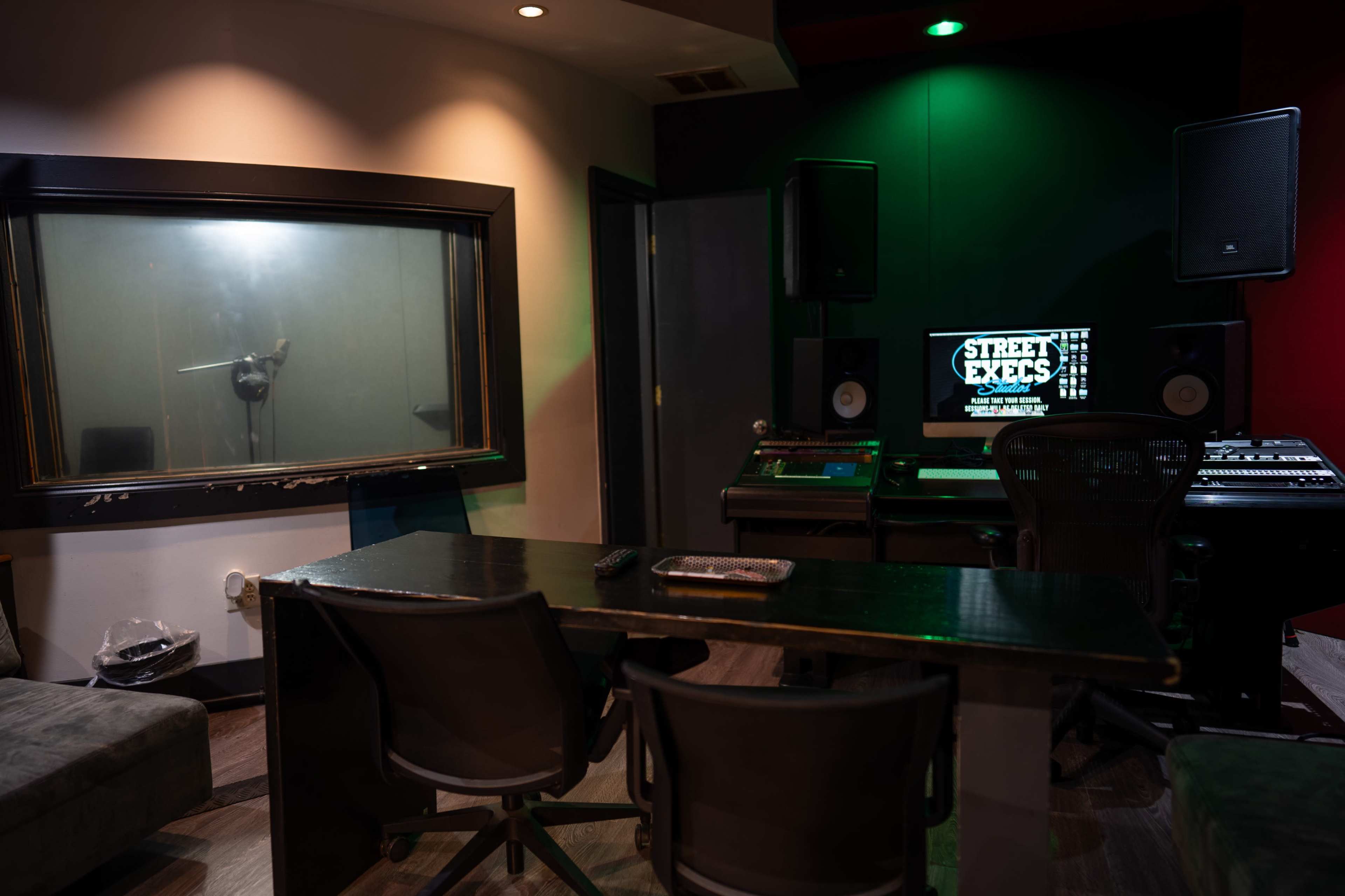 A recording studio with a sound booth, a computer workstation, and a control panel, all set up for audio recording.