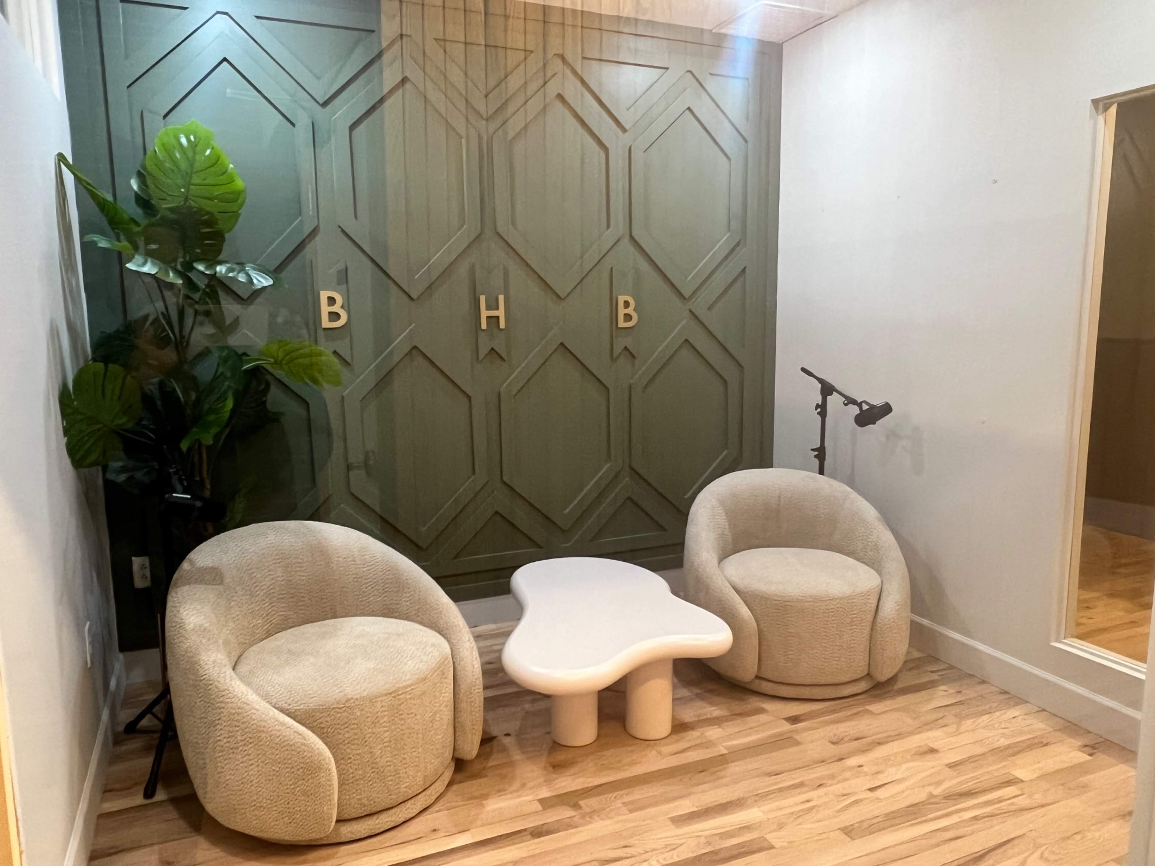 A small waiting area with two round armchairs, a white coffee table, a plant, and a green paneled wall featuring the letters "BHB."