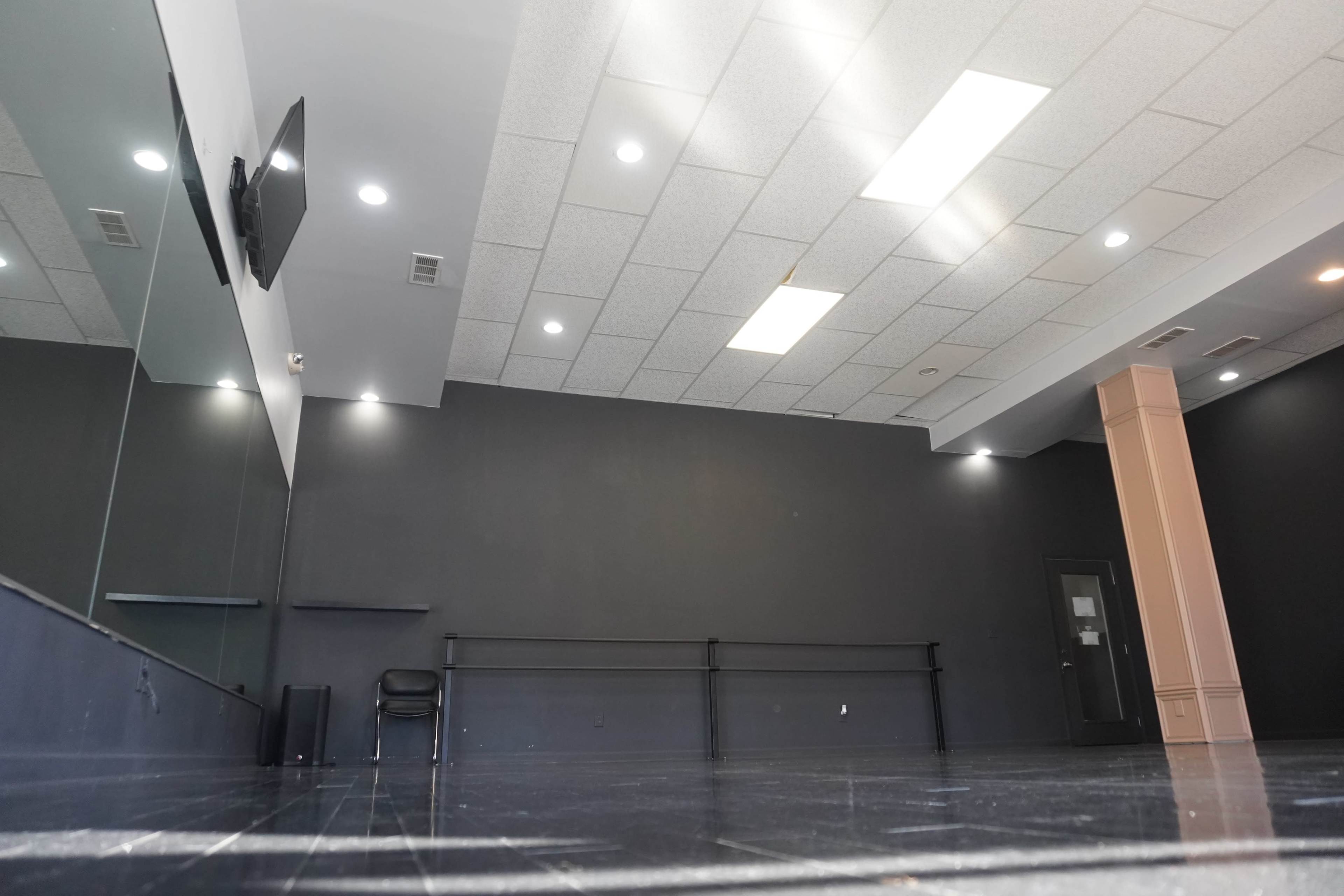 An empty dance studio with mirrored walls, a black floor, and a single chair against one wall.