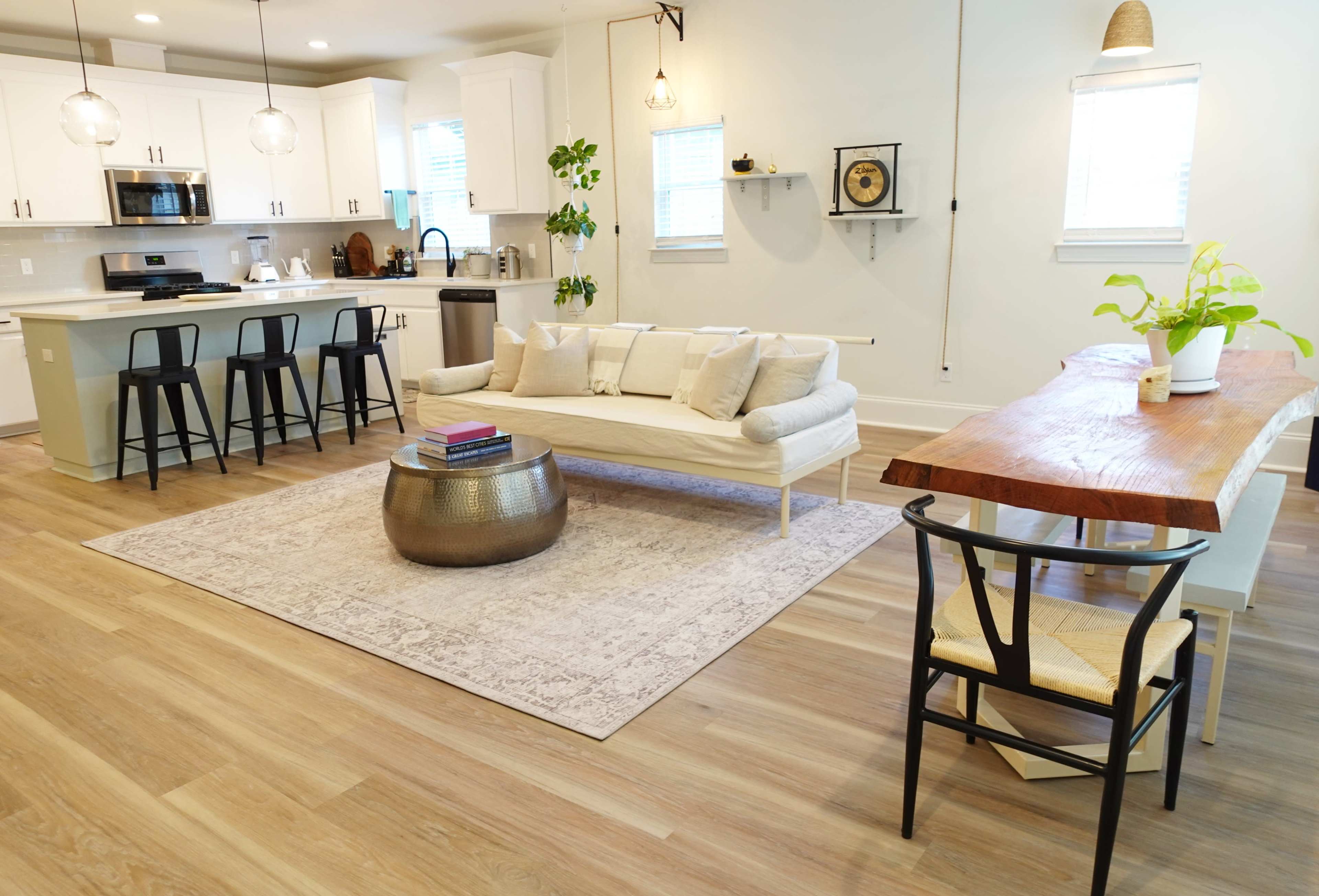 A modern living space with a white sofa, a wooden dining table, and a kitchen area equipped with appliances and bar stools.