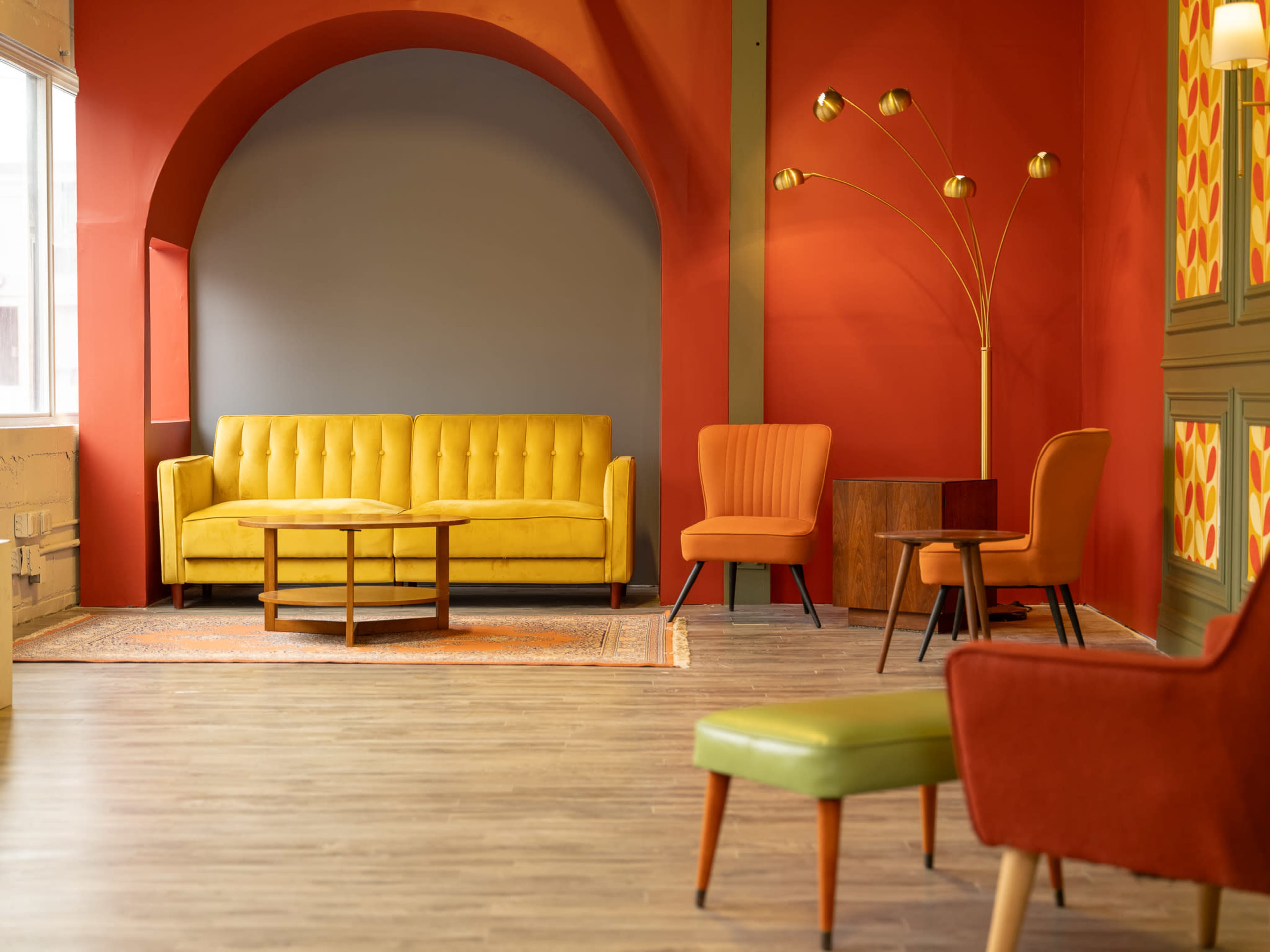 The image shows a brightly colored interior space featuring a yellow couch, two accent chairs, a floor lamp, and patterned wall decor.