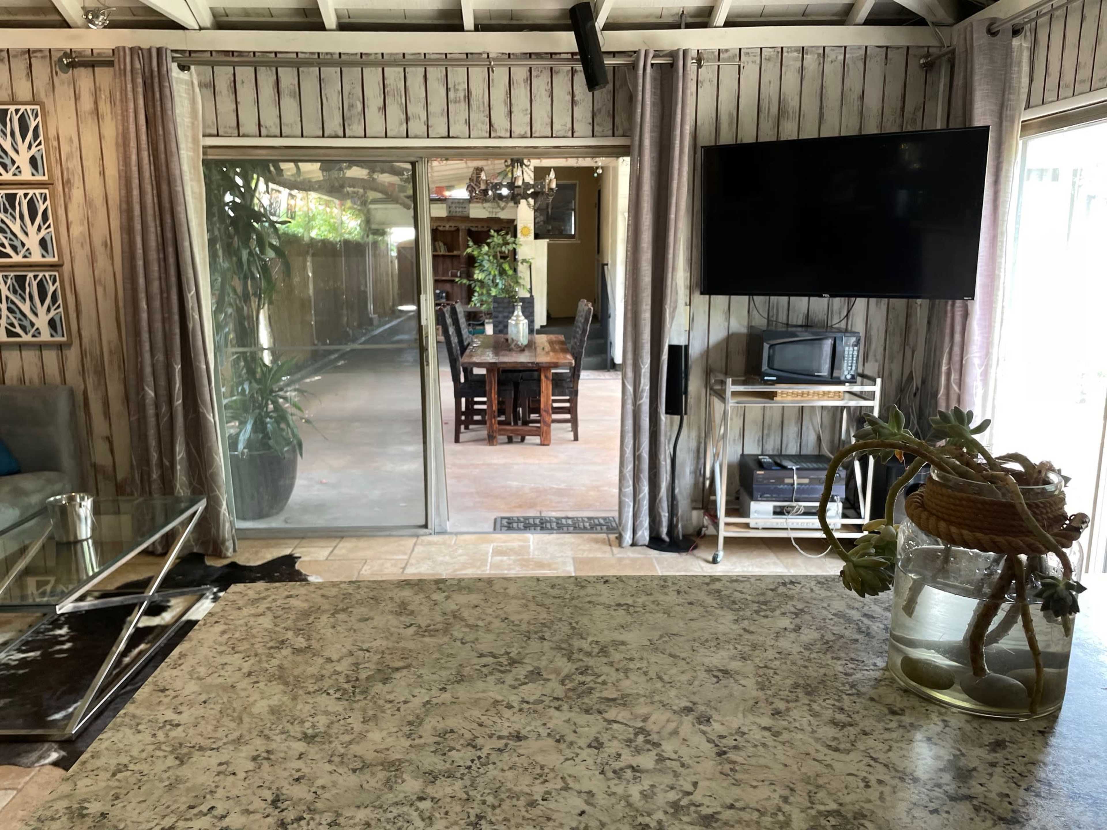 A room with a stone countertop, large sliding glass doors leading to a patio, and a flat-screen TV mounted on the wall.