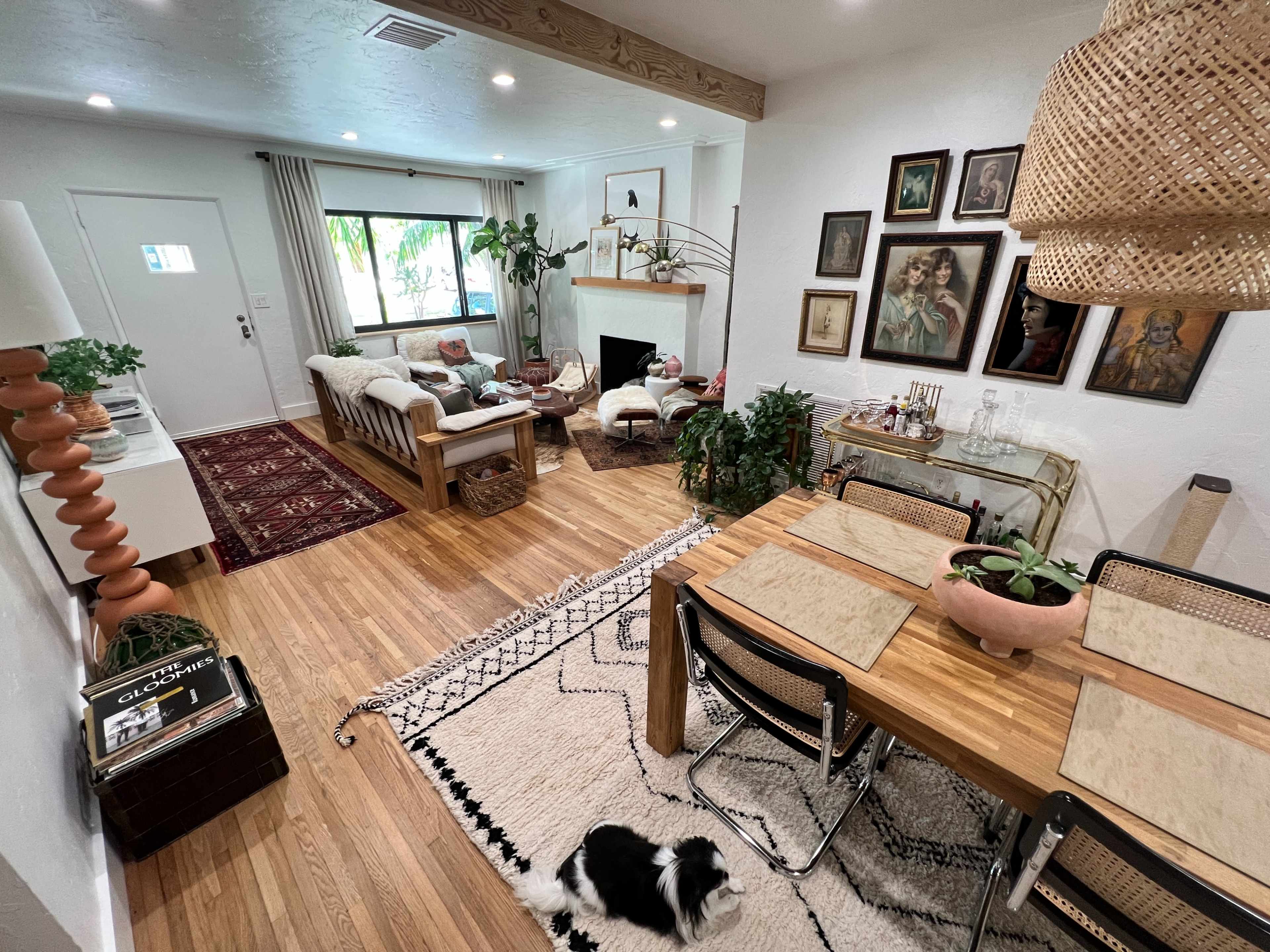 A cozy living and dining area features a mix of plants, artwork on the walls, and a light-colored sofa, with a dining table set for meals.
