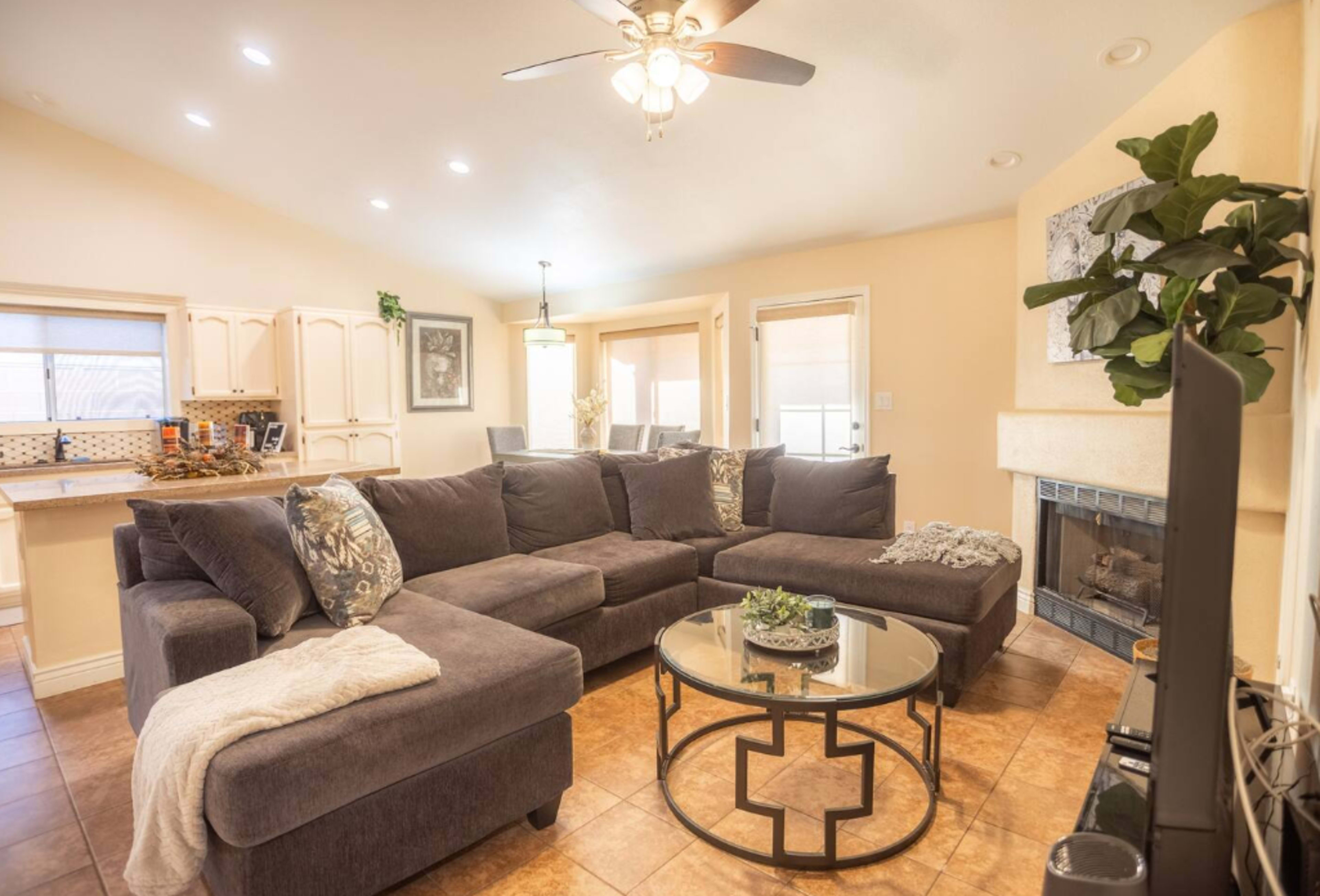 A living room with a sectional sofa, a round coffee table, and a fireplace, with light streaming in from the windows.