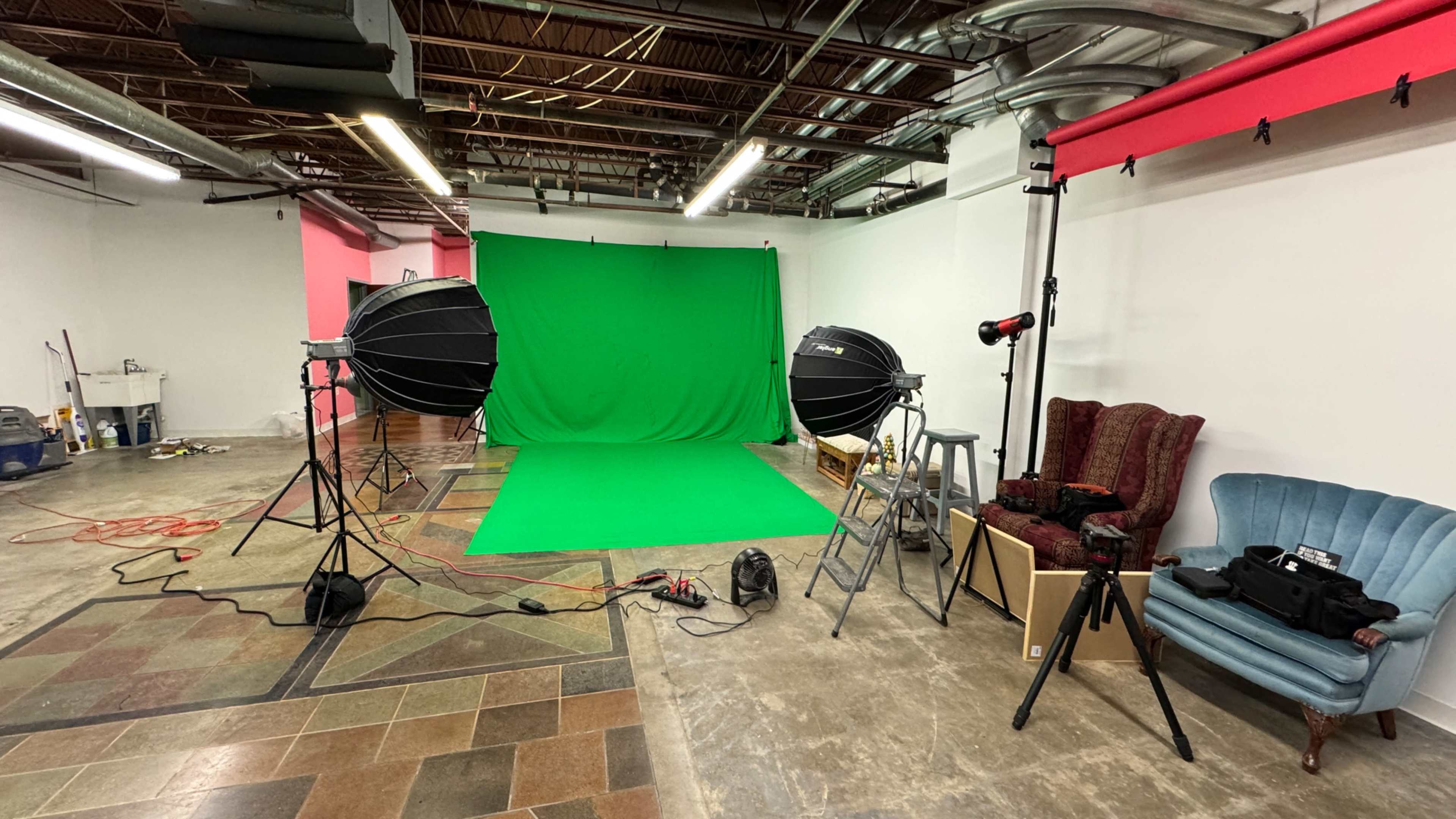 A photography studio setup featuring green backdrop, two large studio lights, and a seating area with two chairs.