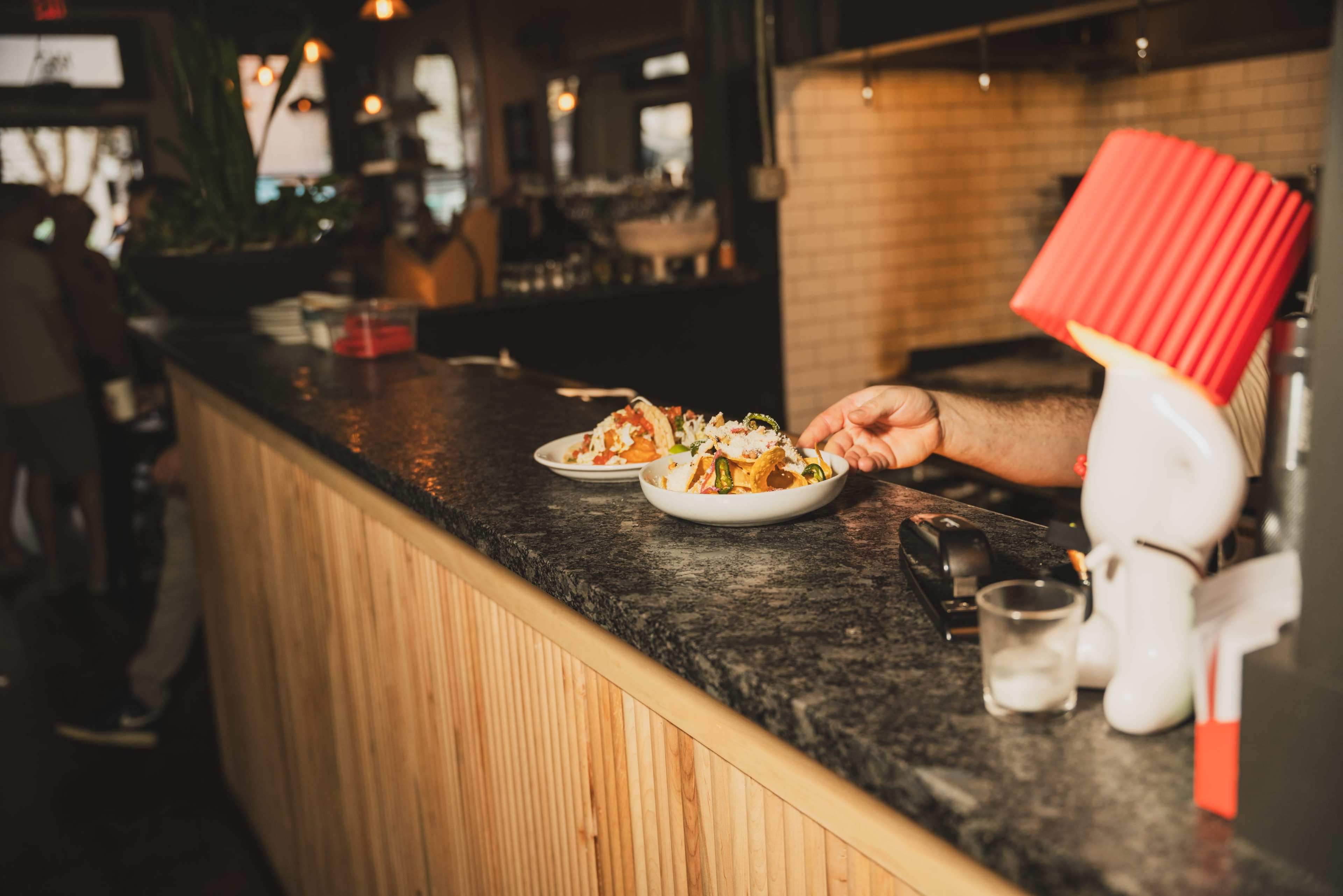 A person is placing two plates of food on a black countertop in a restaurant.