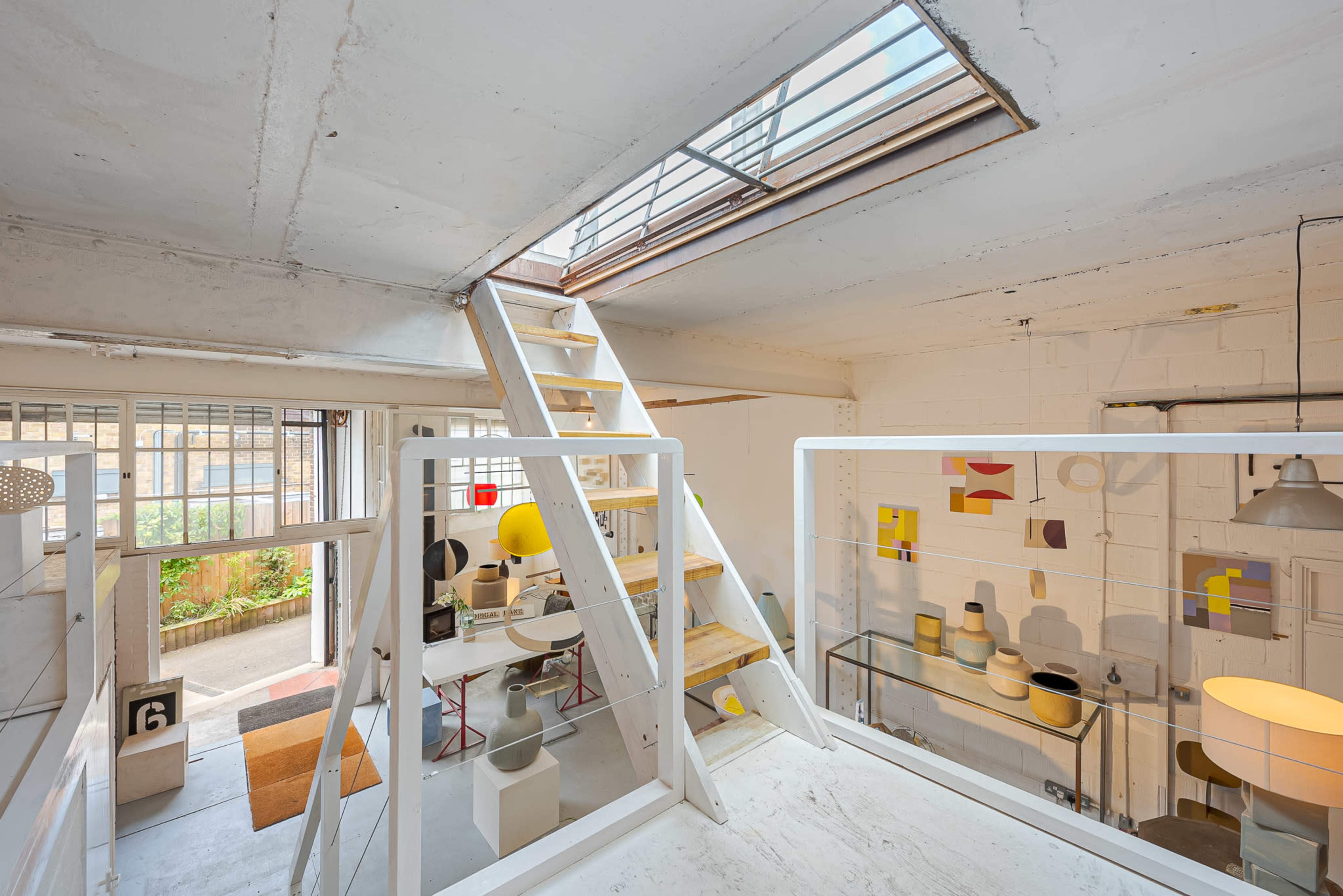A stairway leads to a loft area overlooking a bright, open space filled with various artistic objects and furniture.
