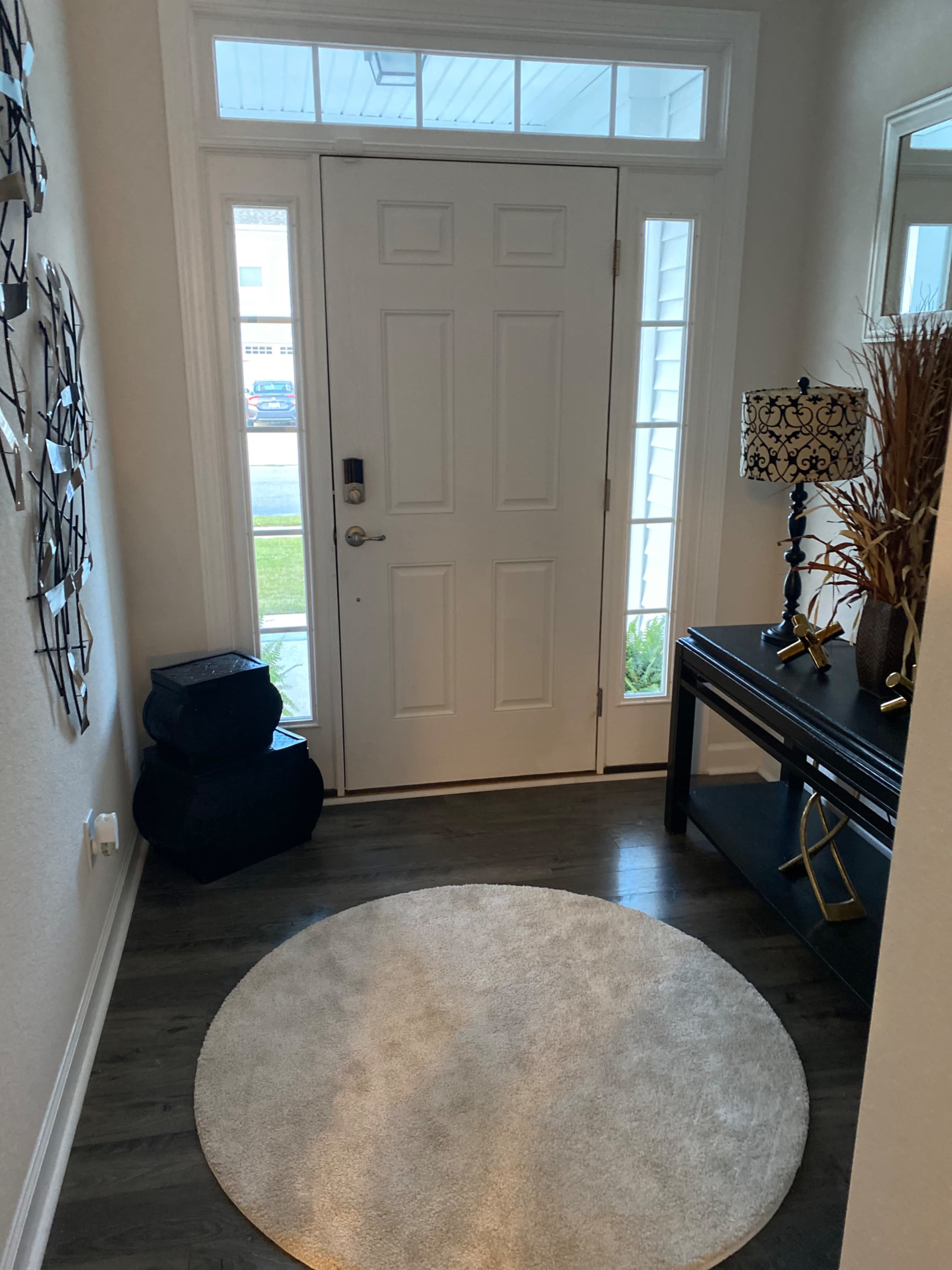 A well-lit entryway featuring a round rug, a console table with a decorative lamp, and a large door with glass panels.