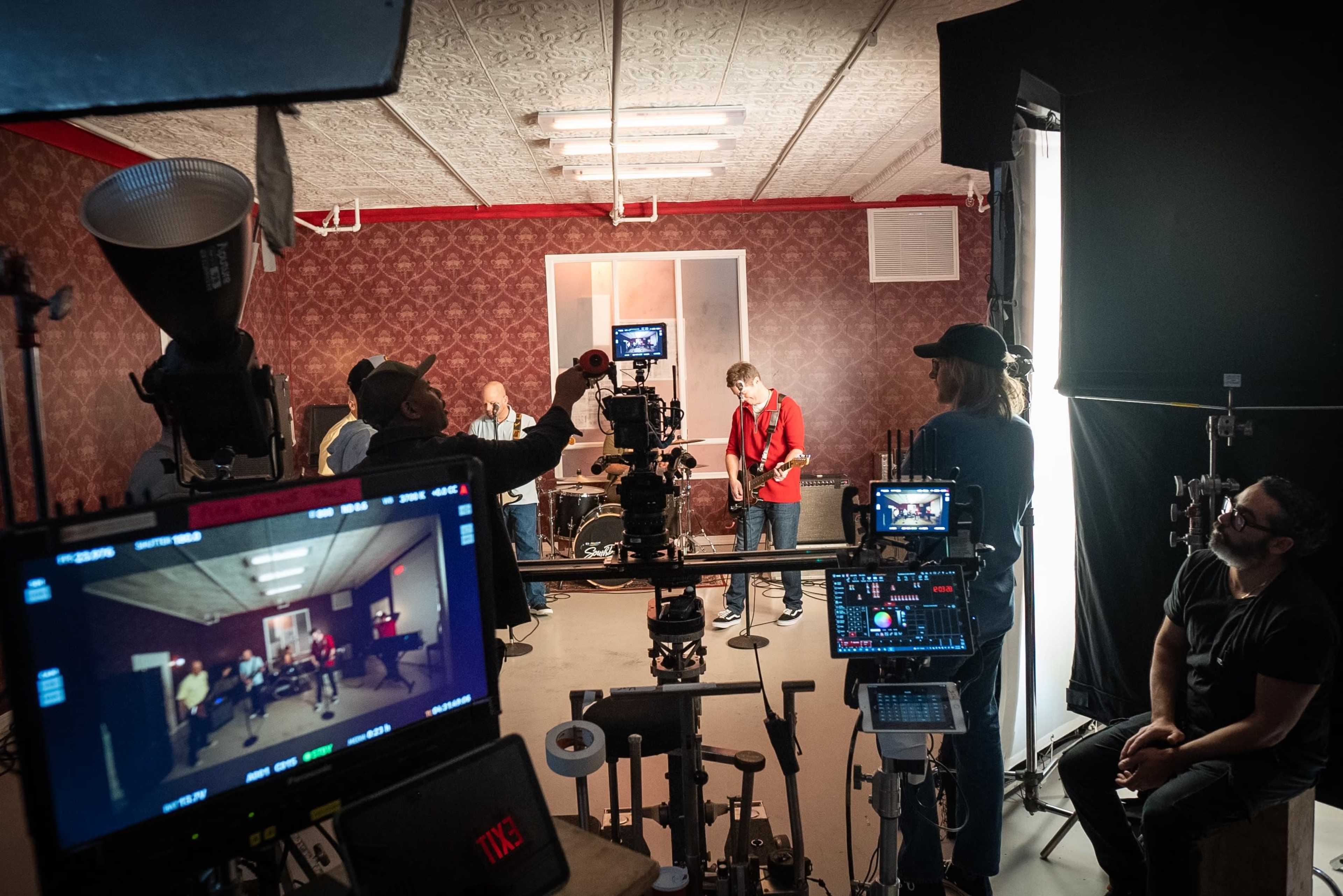 A music video is being filmed in a studio with musicians performing and crew members operating cameras and lights.