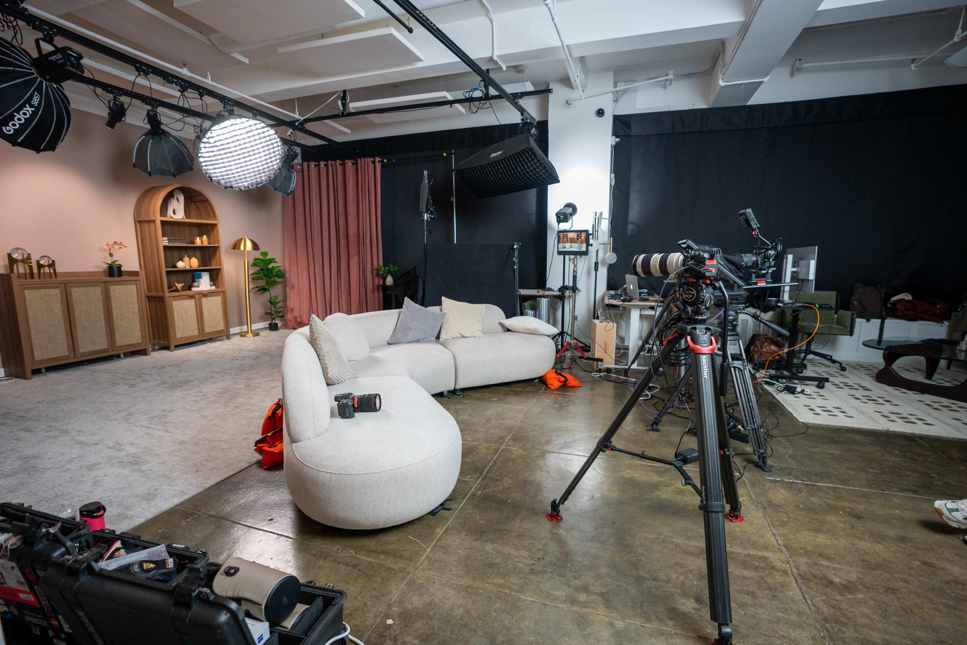 A modern filming studio is set up with a large beige couch, various cameras on tripods, and professional lighting equipment.
