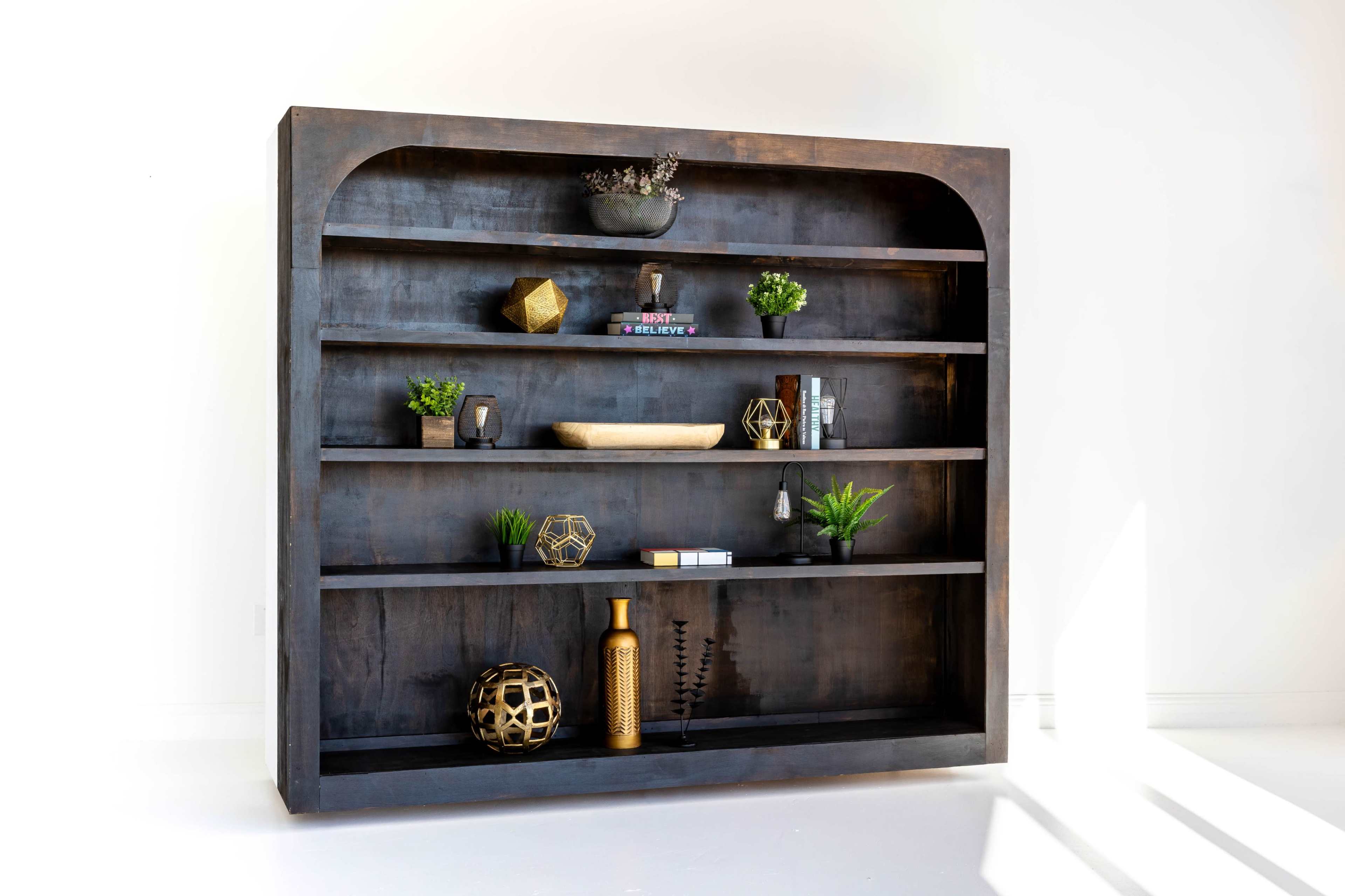 The image shows a dark wooden bookshelf with multiple shelves displaying various decorative items, plants, and books.