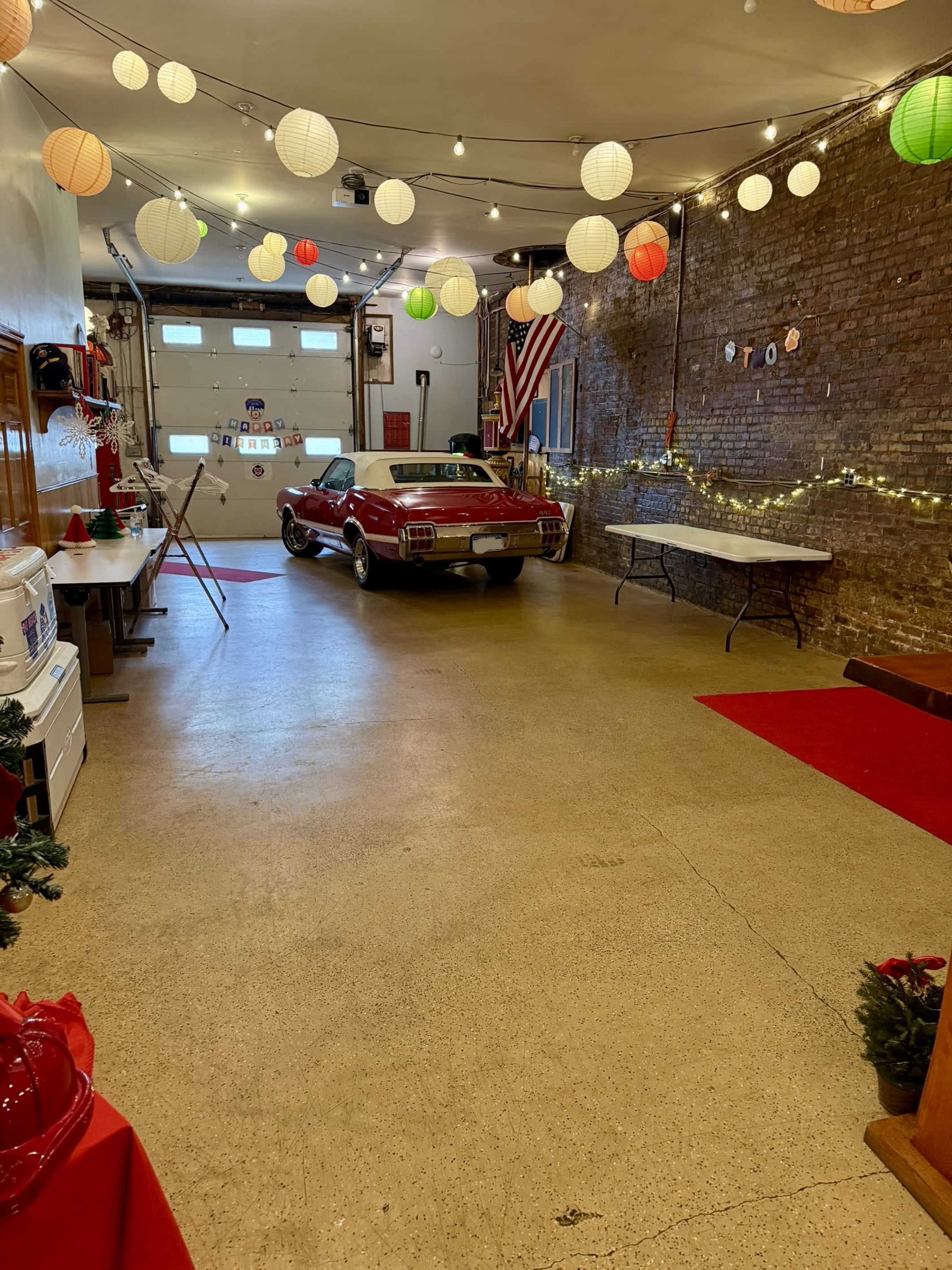 A red car is parked in a decorated garage with colorful paper lanterns and a string of lights along the walls.