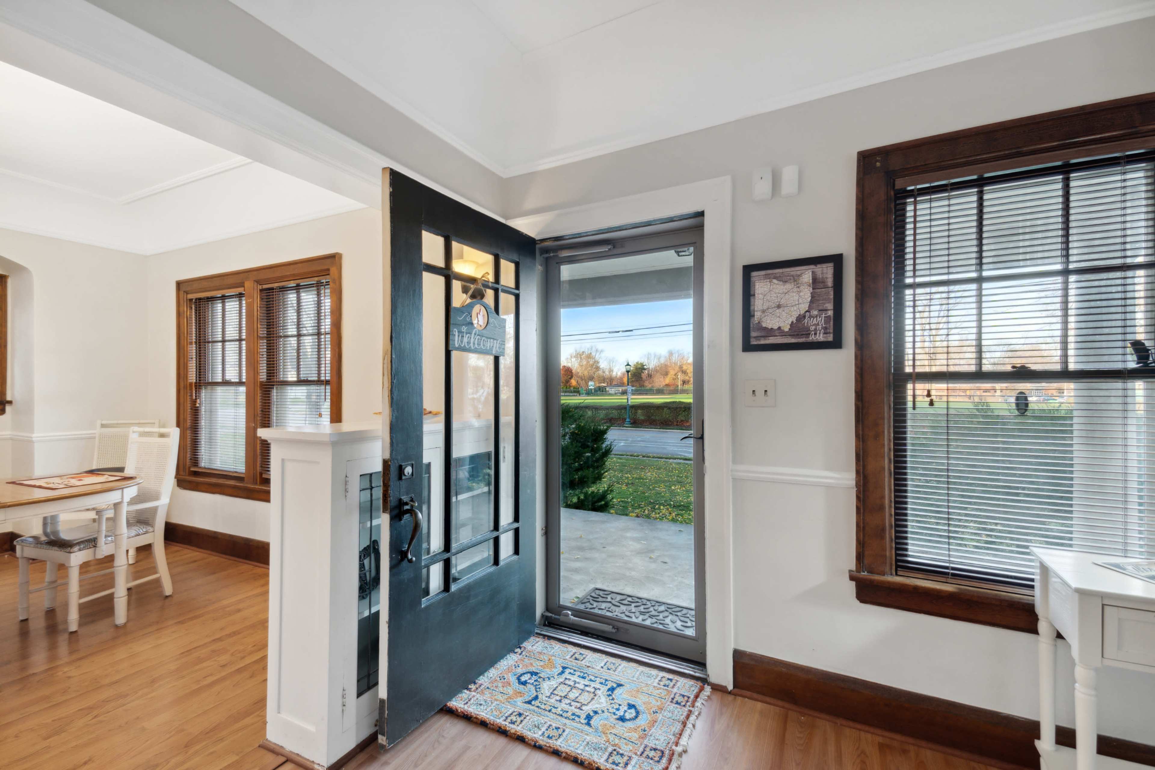 A front entryway features a black door with a window, leading to a porch, with wood trim and a small table nearby.
