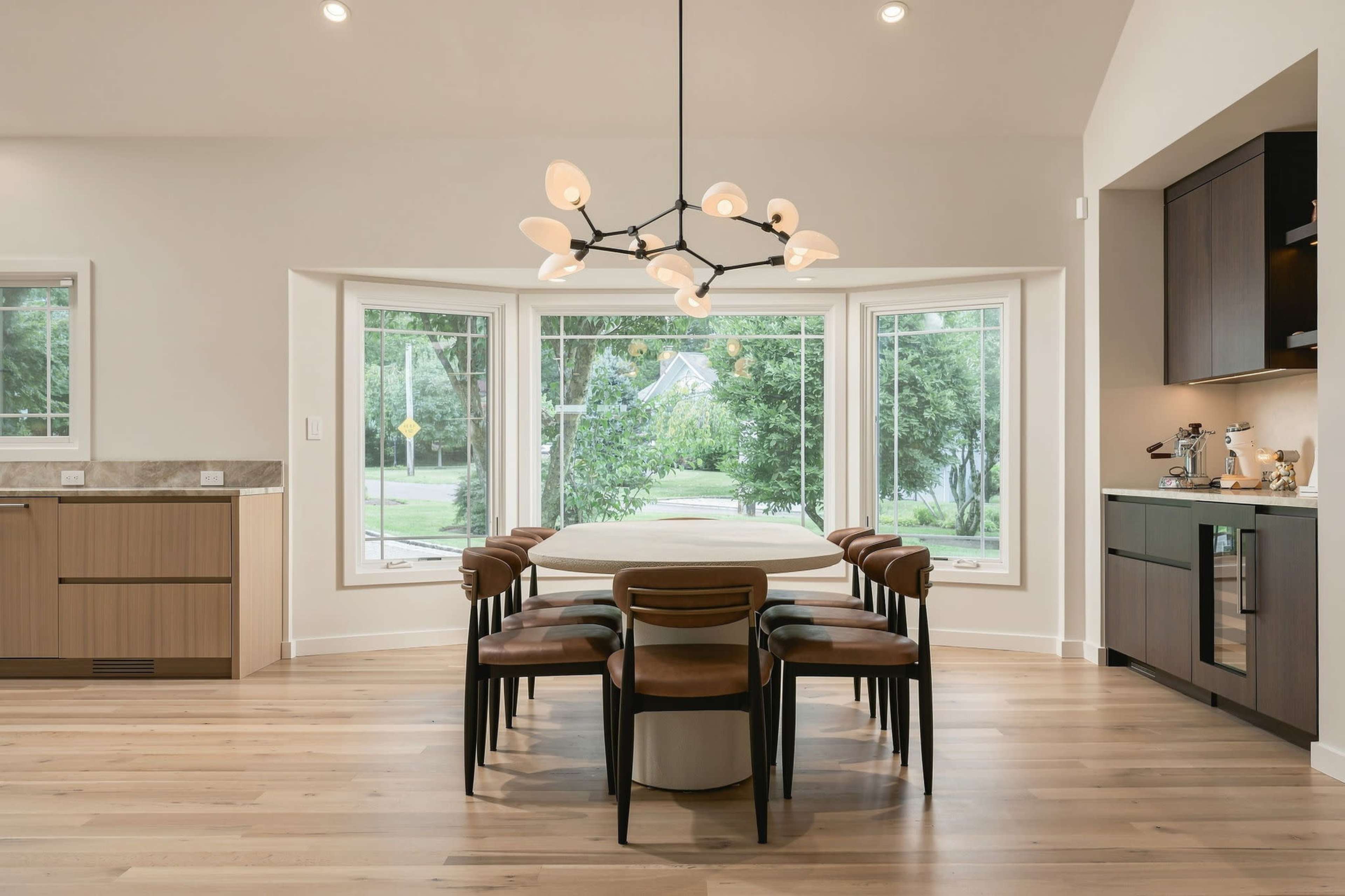 A modern dining area features a round table surrounded by black and wood chairs, with large windows offering views of the outdoors.