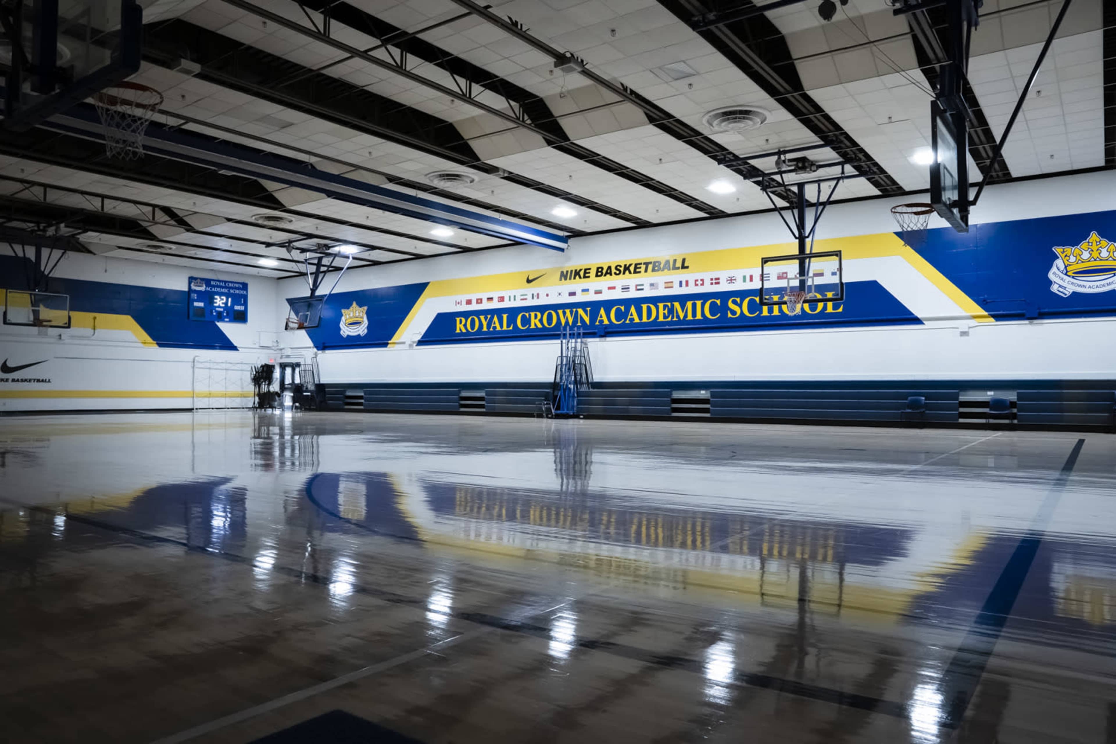 The image shows a basketball gymnasium with polished wooden floors, blue and yellow walls, and a scoreboard displaying a score of 32.