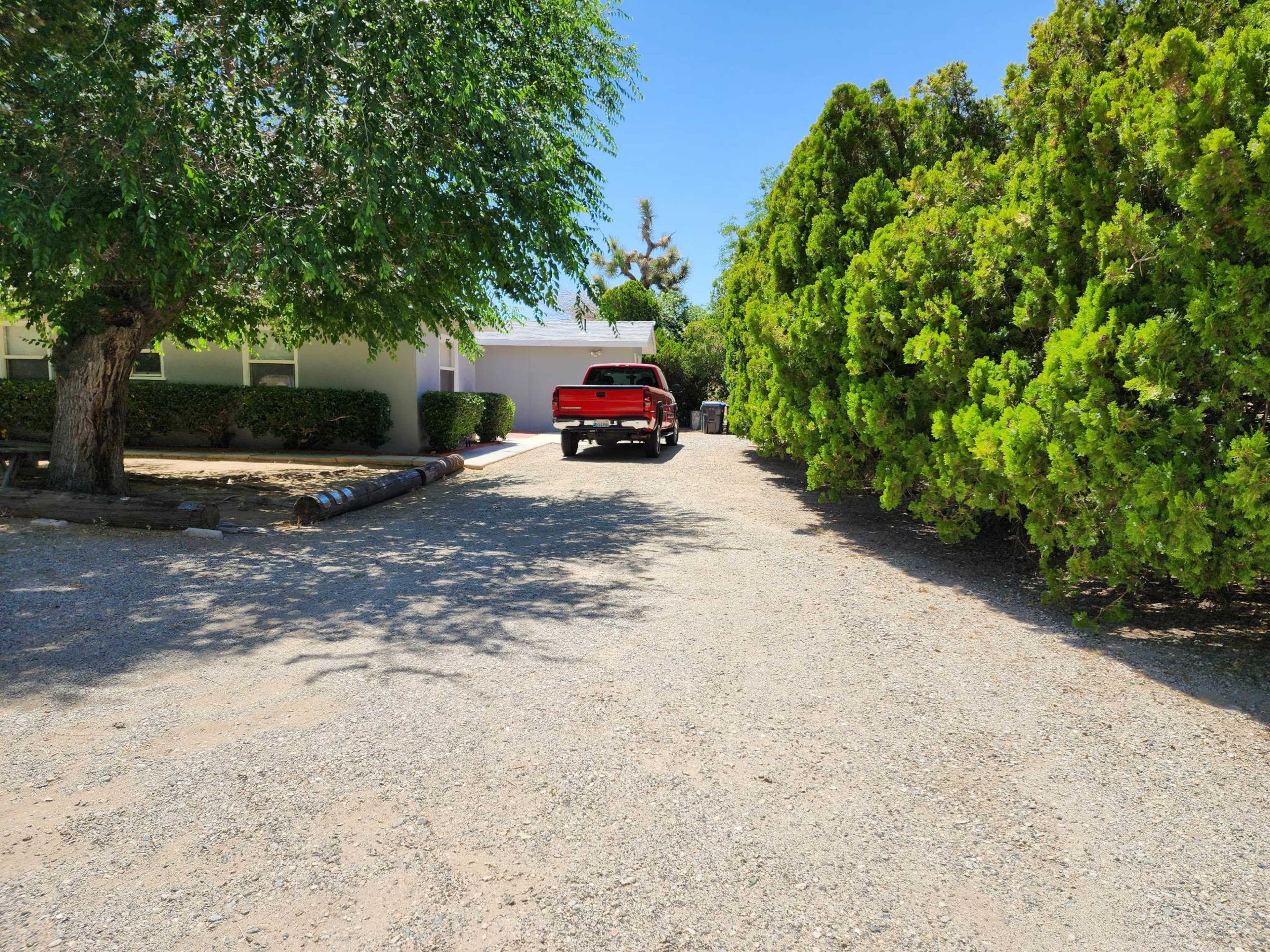 A red truck is parked on a gravel driveway surrounded by greenery and trees.