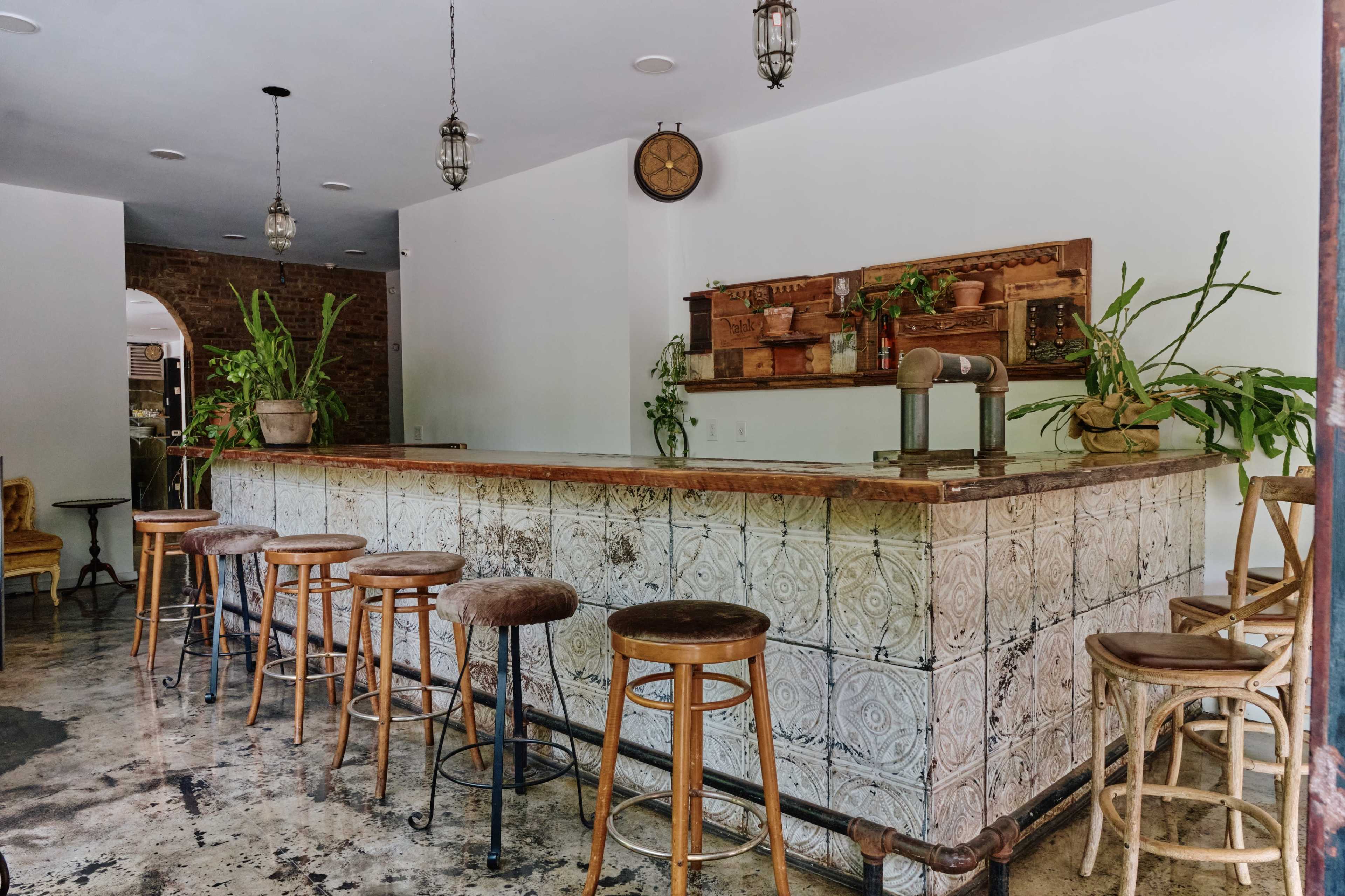 A spacious bar area features a tiled counter and wooden stools, surrounded by indoor plants.
