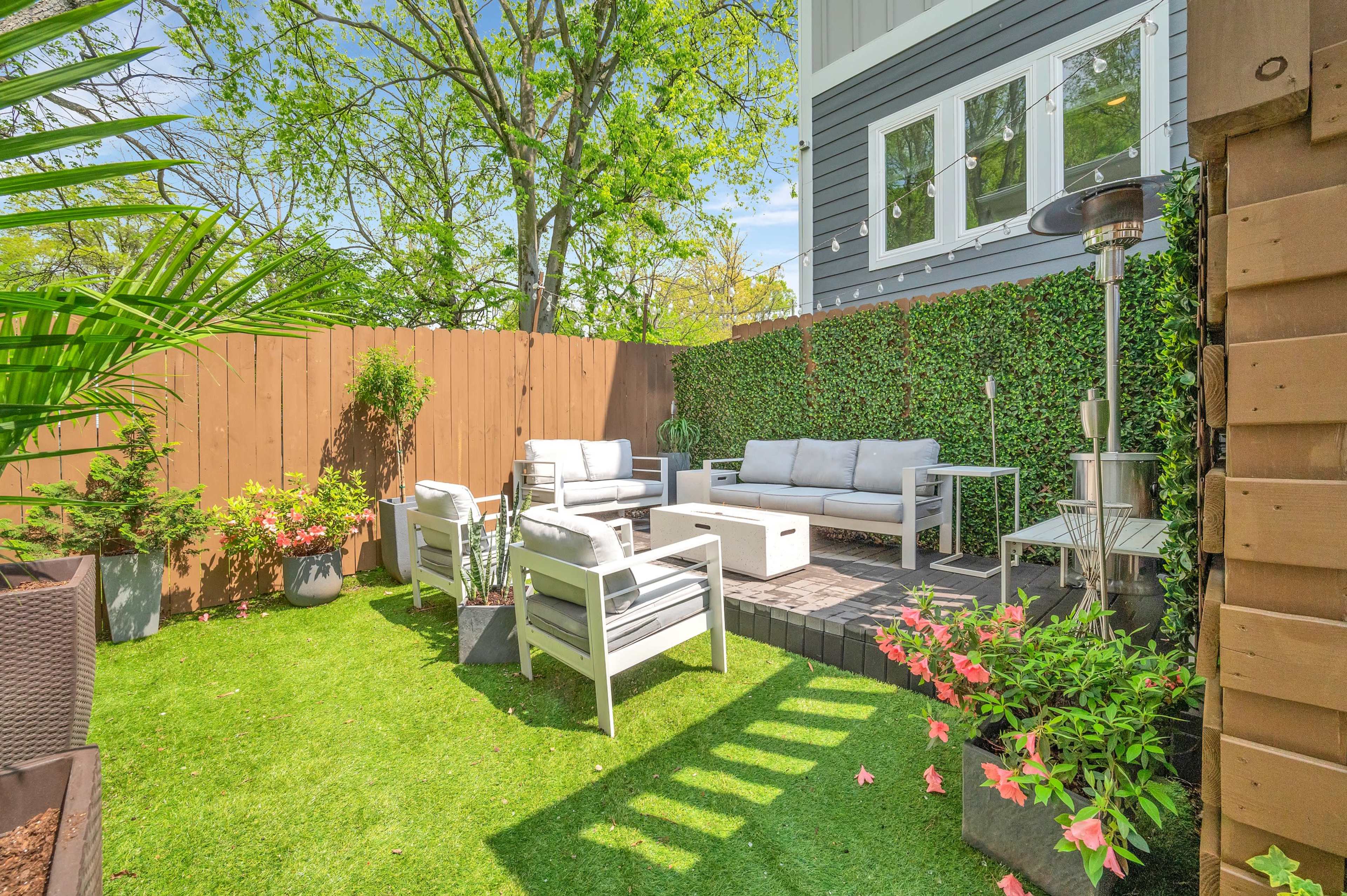 A landscaped outdoor seating area with white patio furniture, greenery, and a wooden fence.