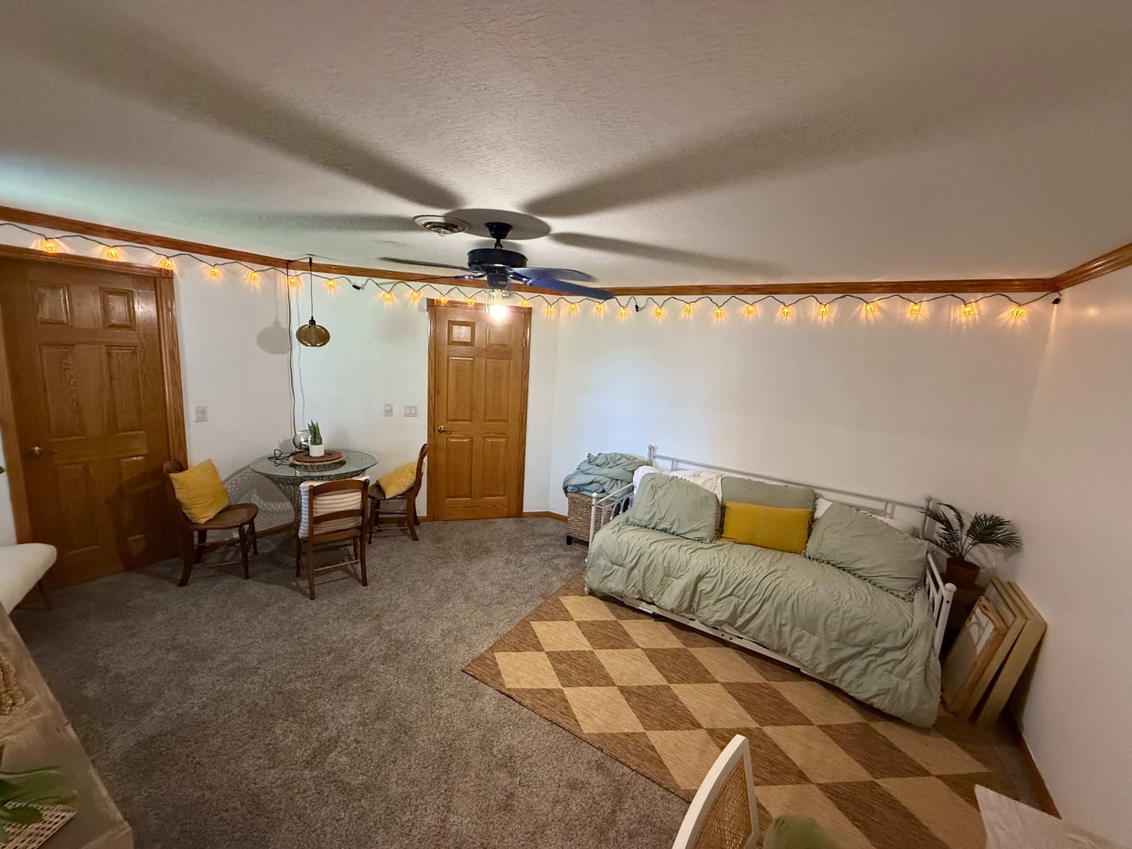 The image shows a cozy room with a couch, a dining table with chairs, and warm string lights adorning the walls.