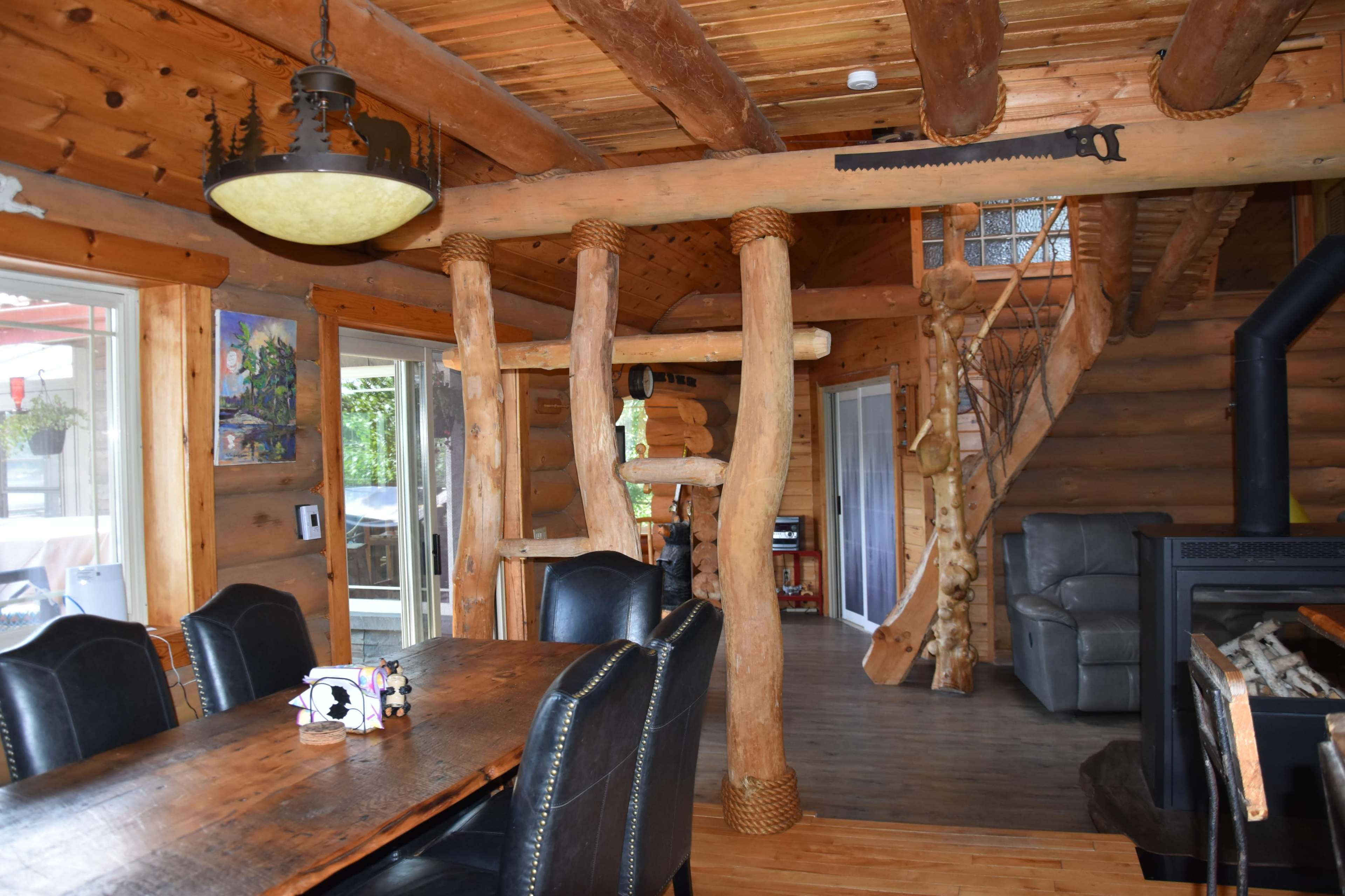 The interior of a log cabin featuring wooden beams, a dining table, and a staircase leading to the upper level.