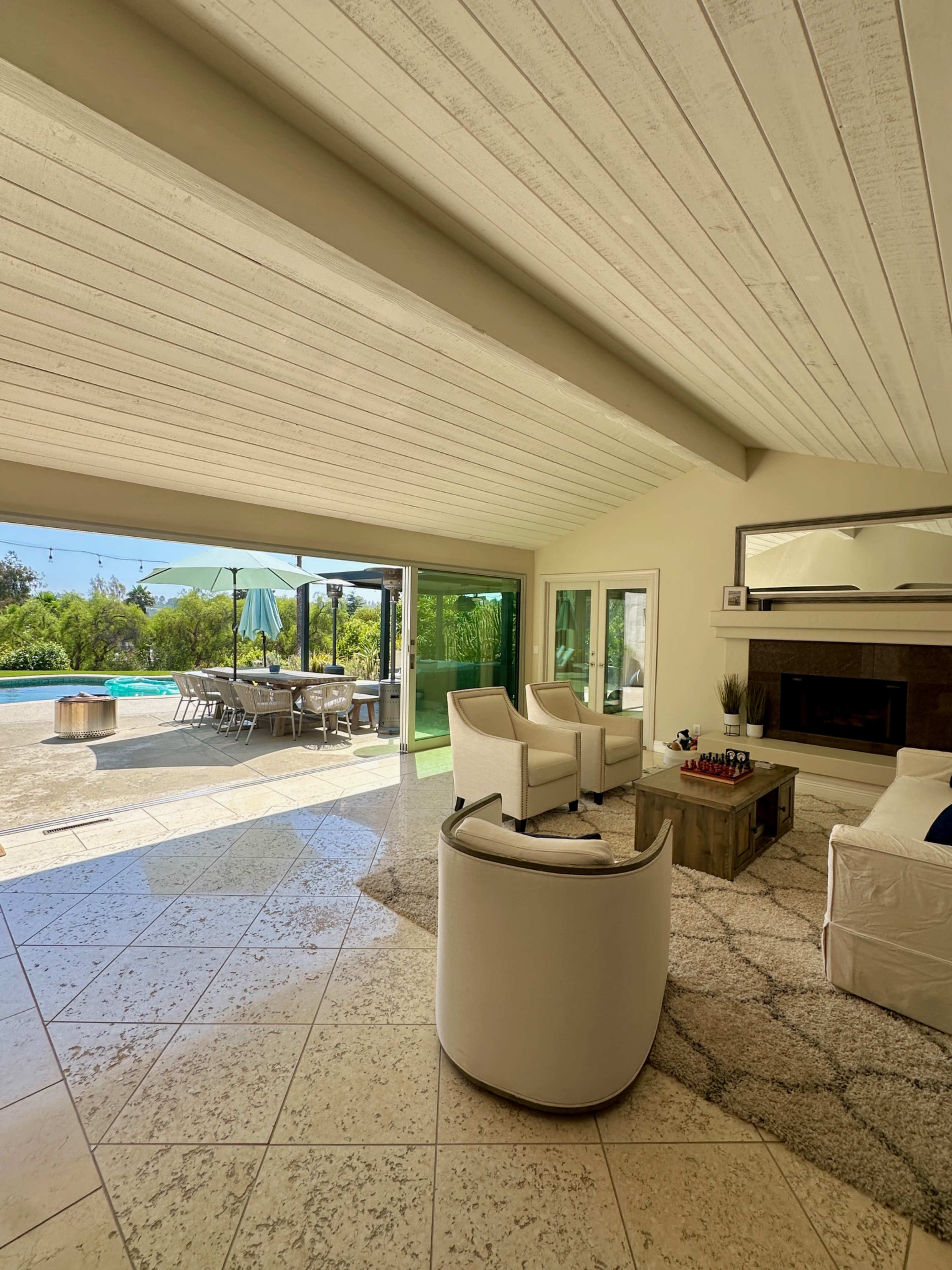 The image shows a modern, open-concept living area with a view of a patio and pool, featuring comfortable seating and a coffee table.