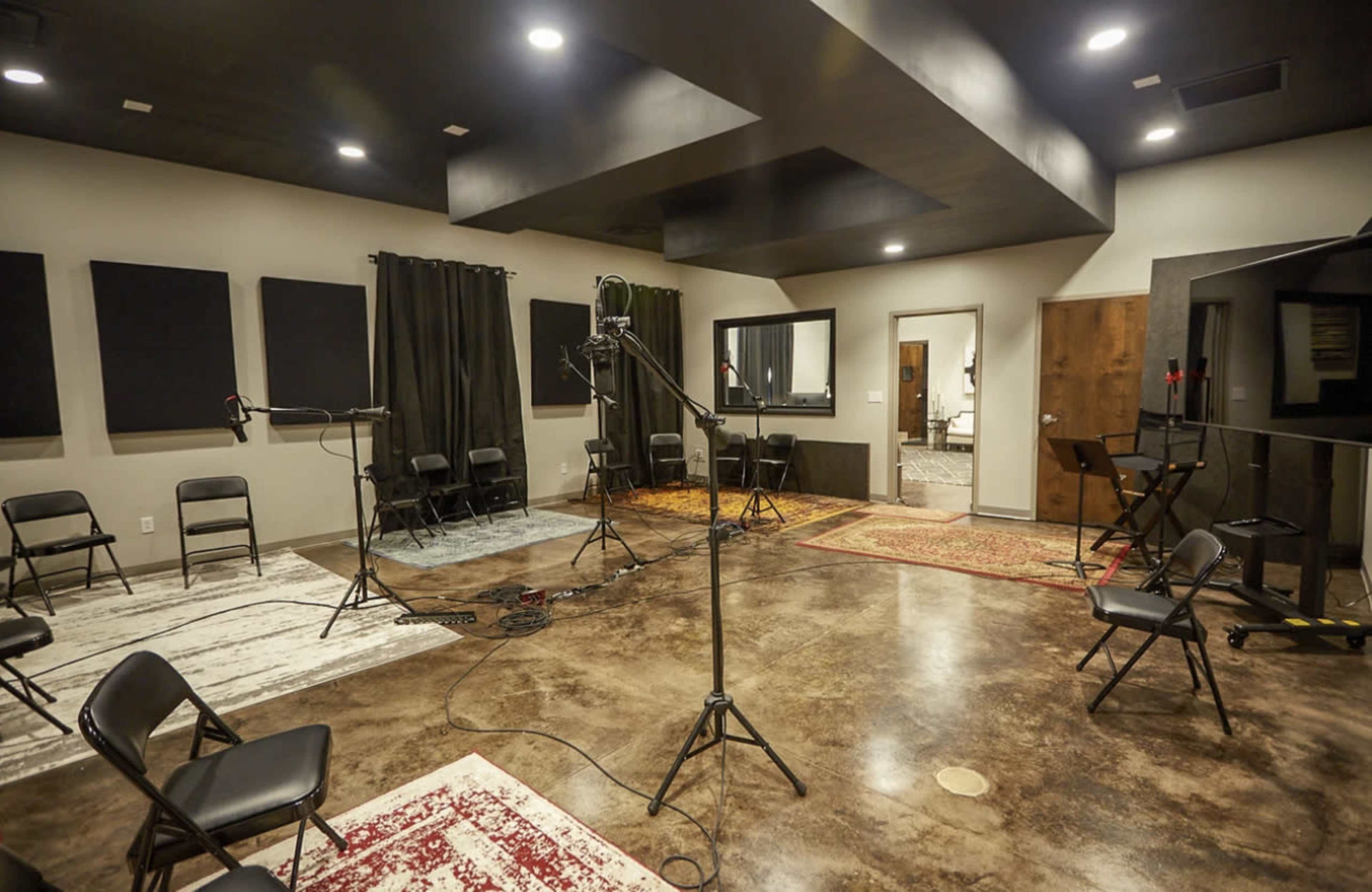 A recording studio with several chairs arranged around a central area, soundproof panels on the walls, and microphones on stands.