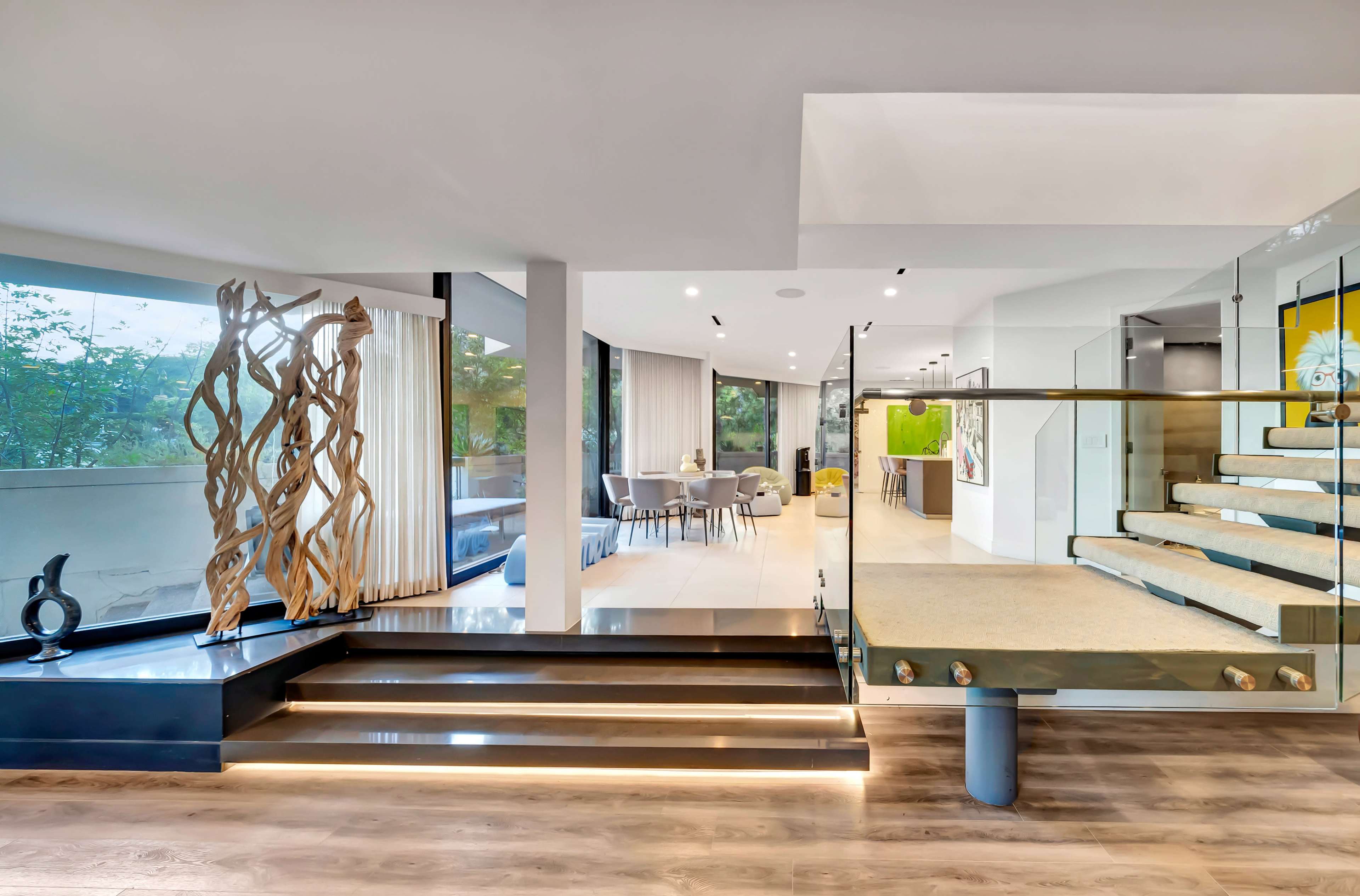 The image shows a modern, open-concept living space featuring a staircase, large windows, and a decorative wooden sculpture.