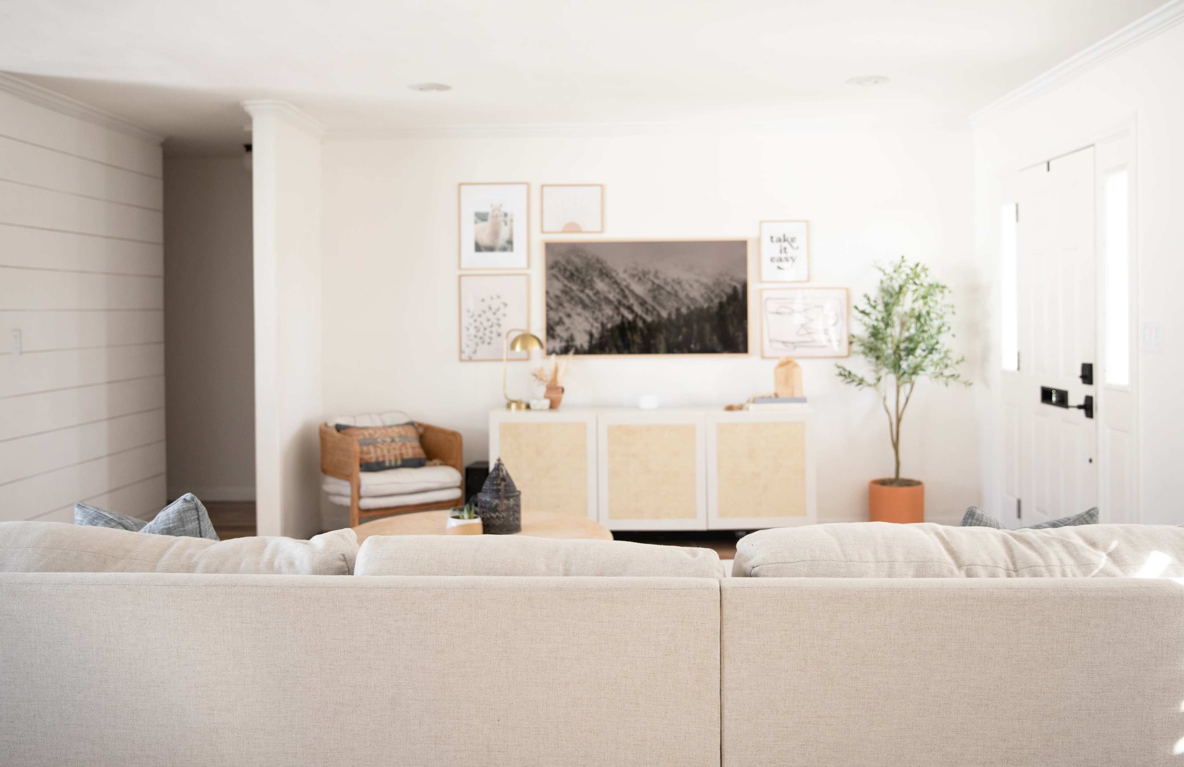 A cozy living room features a light-colored sectional sofa facing a media console with framed artwork on the wall behind it.