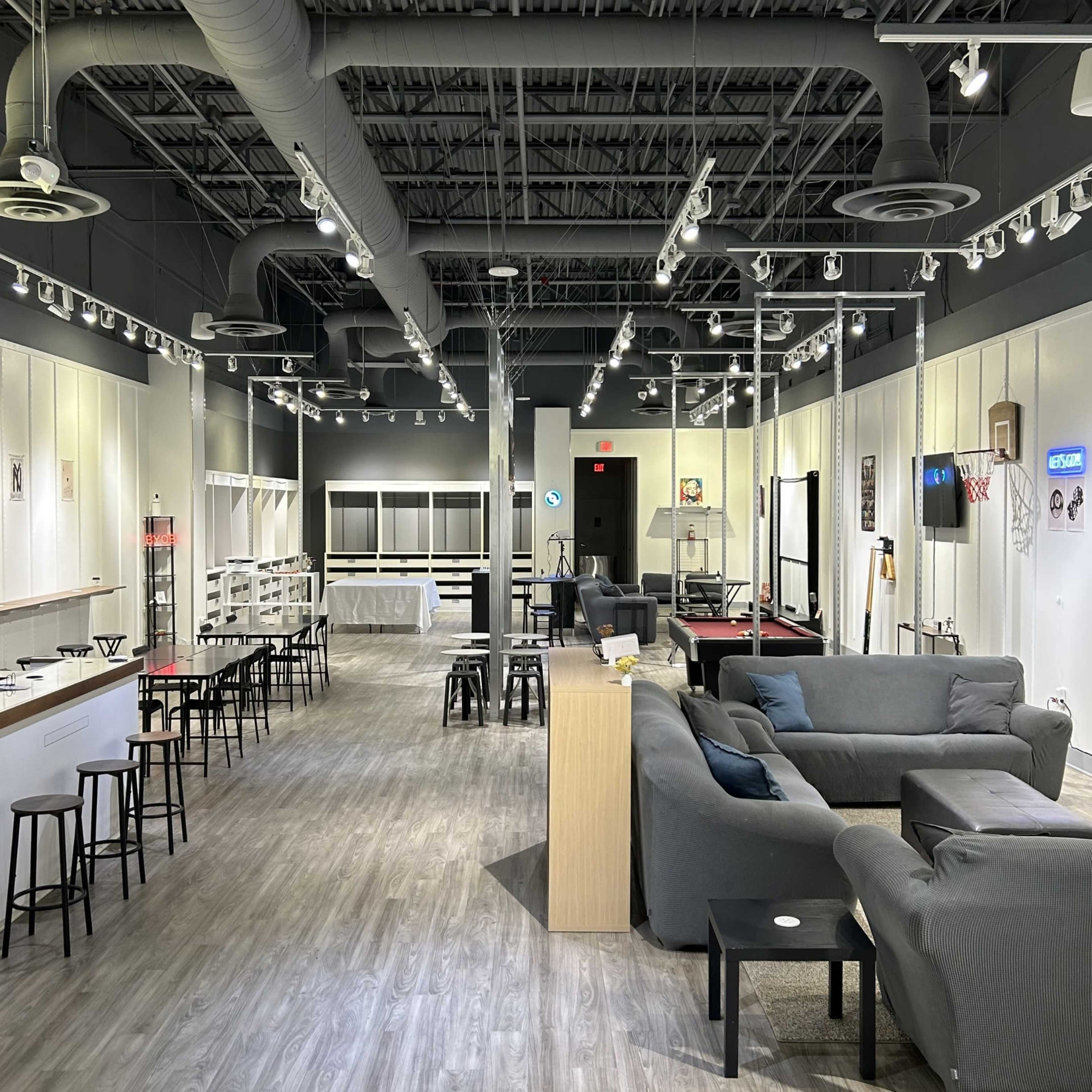 The image shows a spacious indoor recreational area furnished with seating, games, and a bar setup.